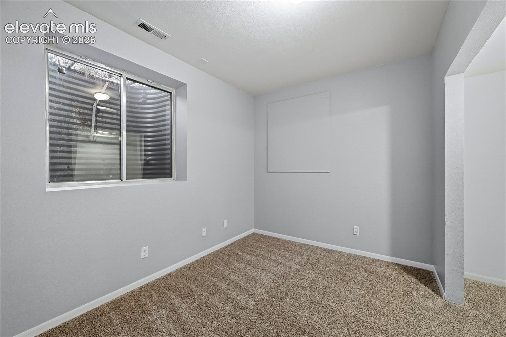 Neutral-toned room featuring neutral-toned carpeting, light gray walls, and an egress-style window with a corrugated steel window well