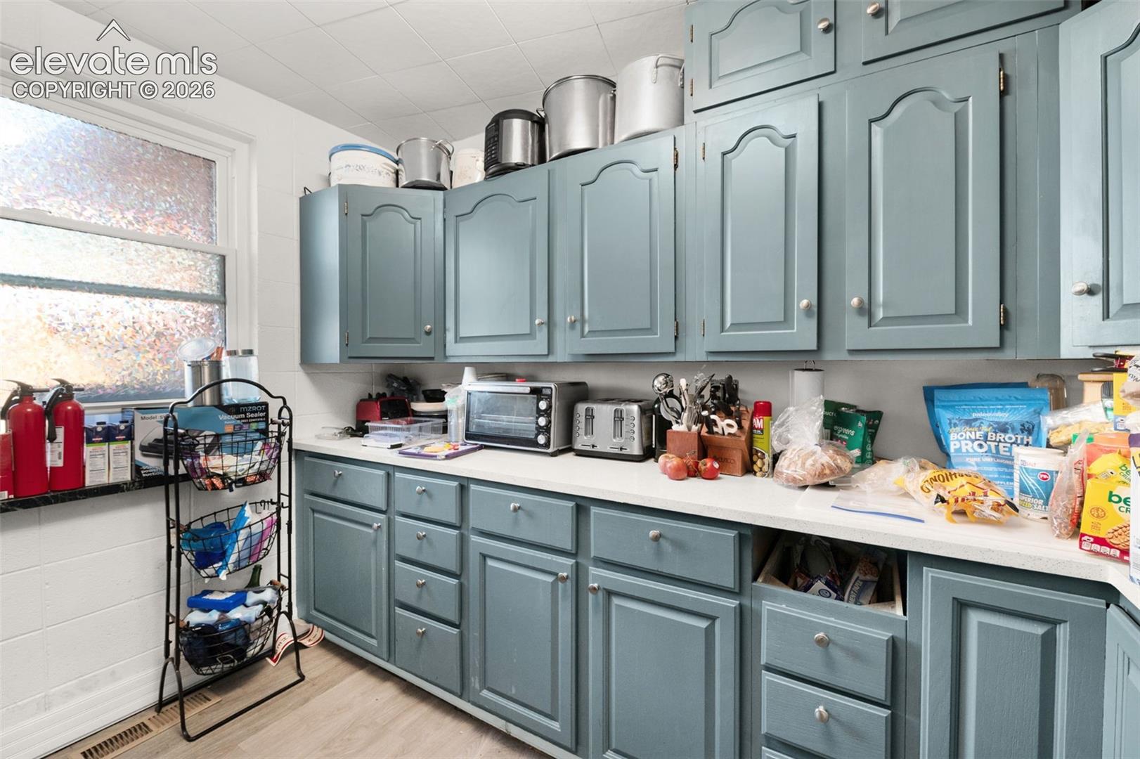 Kitchen featuring slate blue cabinetry with arched-panel doors, neutral solid-surface countertops, and a single-hung window