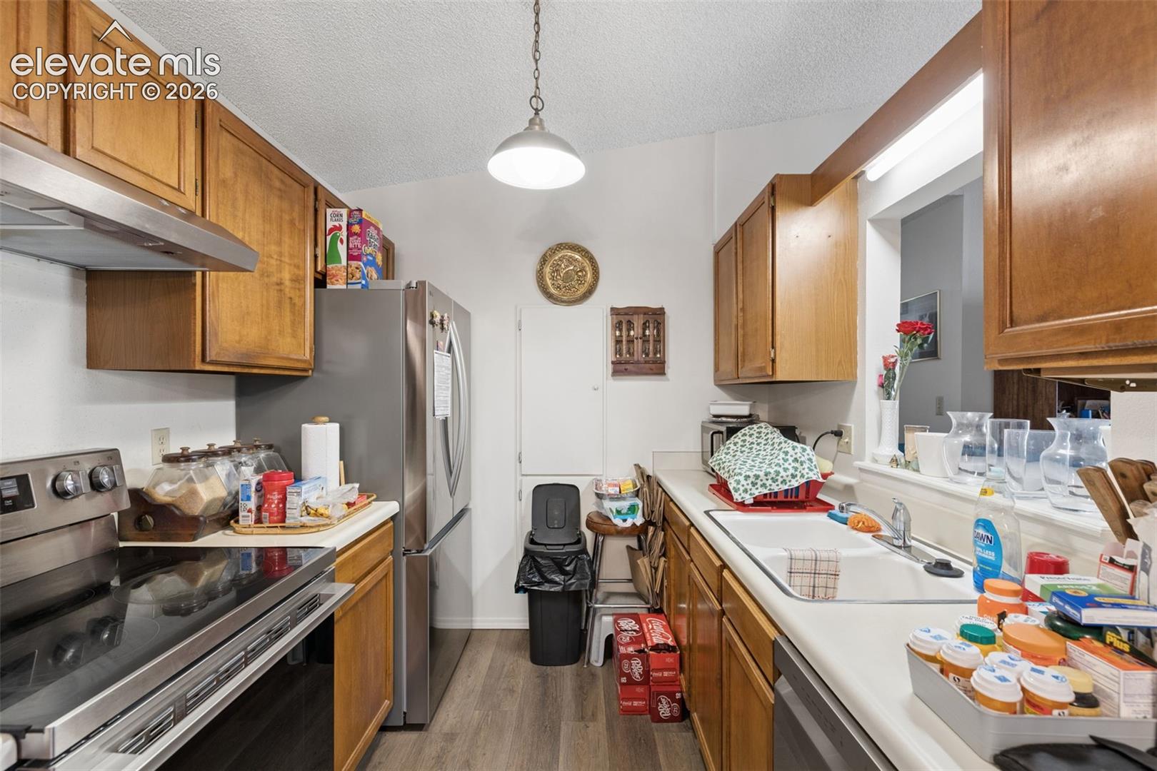 Kitchen featuring wood cabinetry, stainless steel appliances, a dual-basin white sink with a metal faucet, and wood-finish flooring