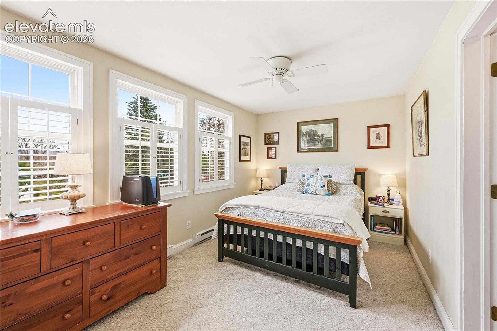 Neutral-toned room featuring three multi-pane windows with integrated plantation shutters, wall-to-wall carpeting, and a ceiling-mounted fan