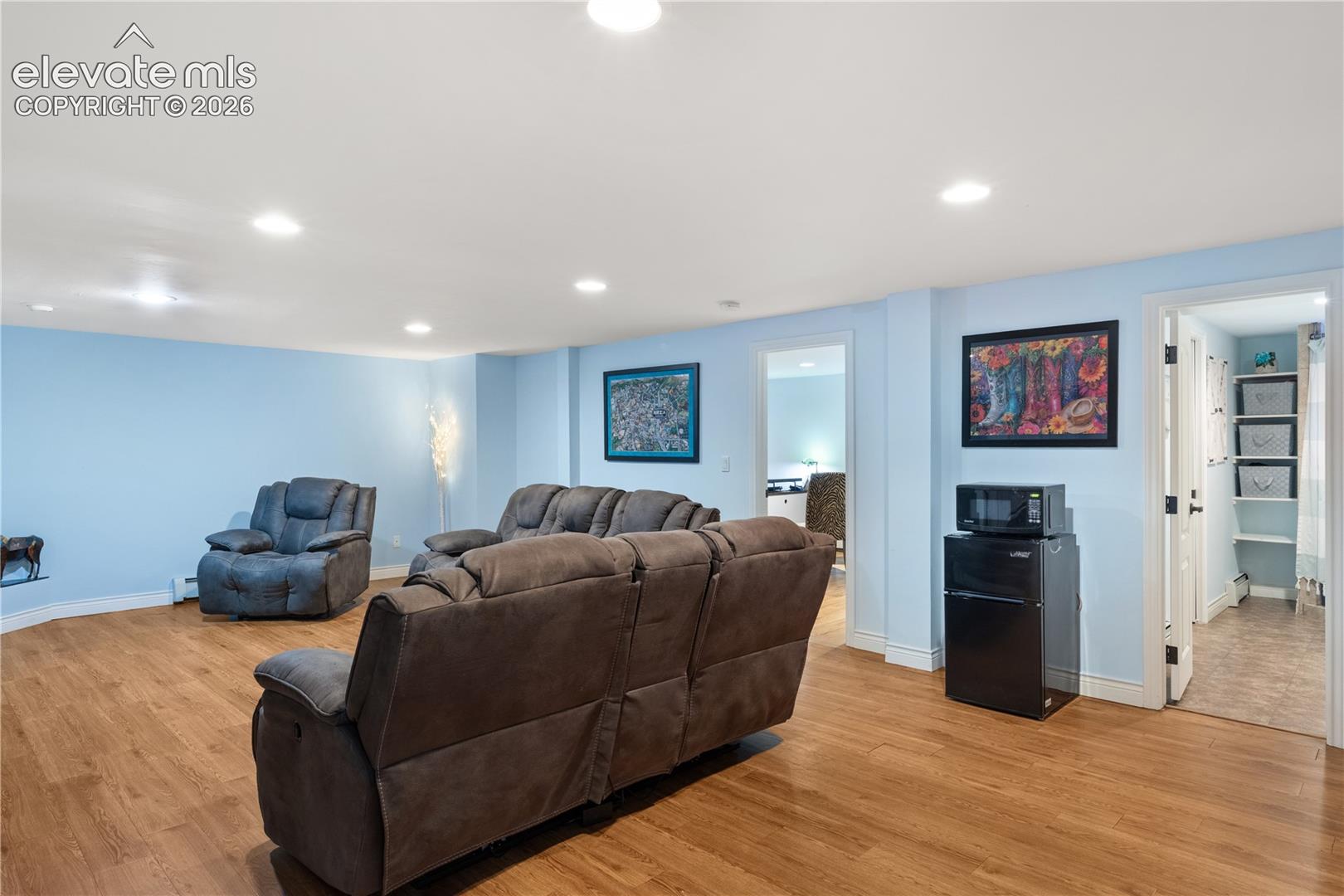Recessed lighting illuminates the spacious room featuring wood-finish flooring and light blue walls