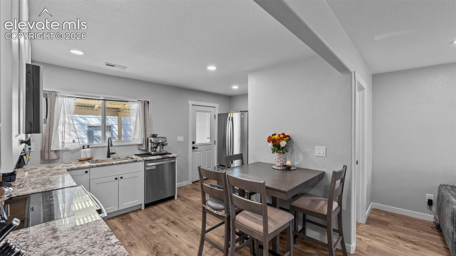 Kitchen featuring white cabinetry, stone-patterned countertops, wood-finish flooring, recessed lighting, and a stainless steel dishwasher