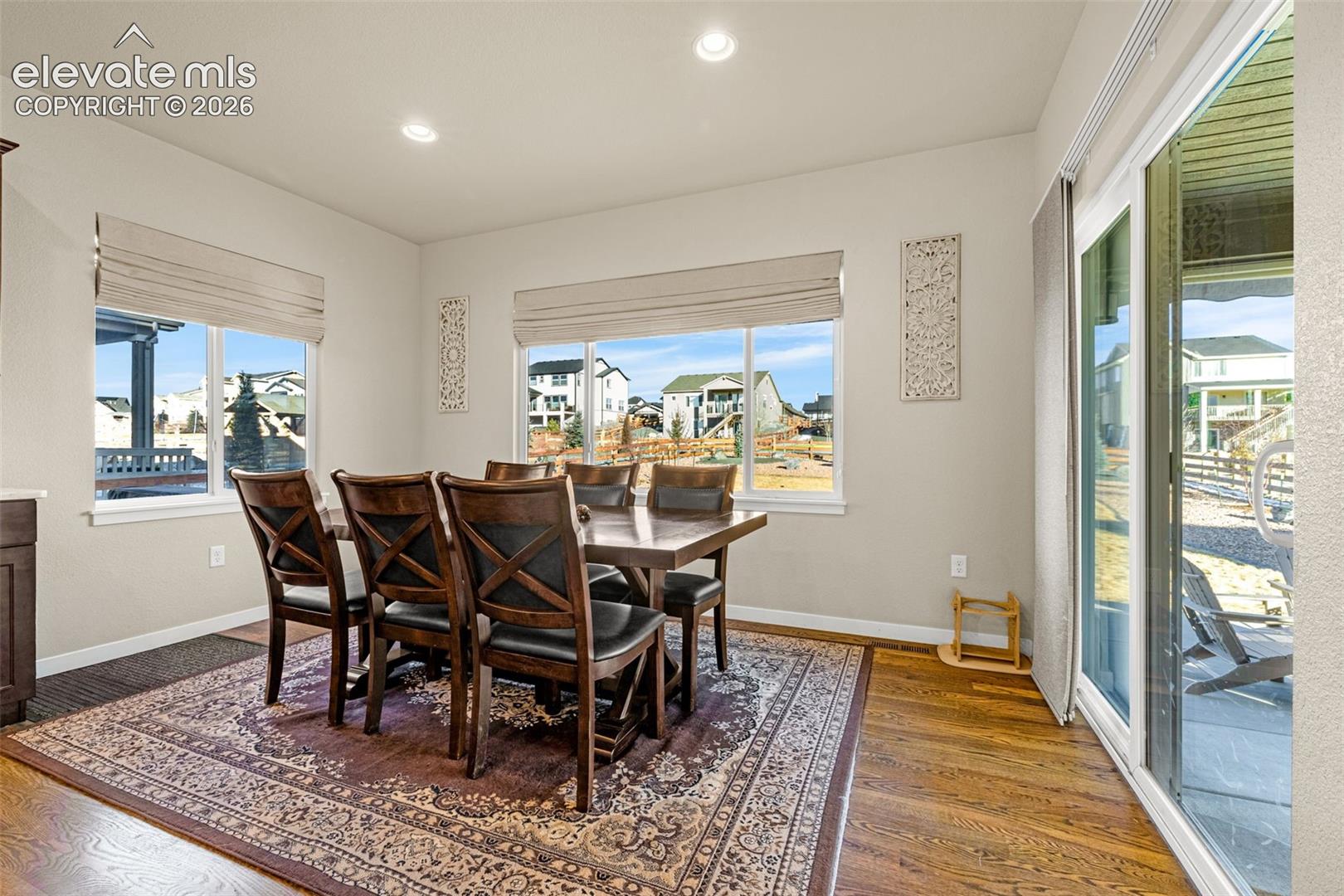 Dining area featuring wood-finish flooring, recessed lighting, and expansive windows with neutral-toned fabric shades