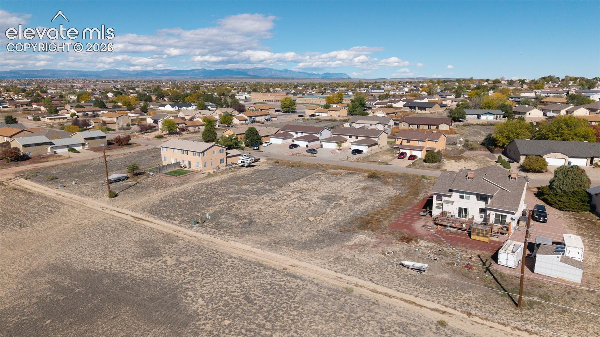 Aerial perspective of an expansive land parcel featuring a multi-story residence with a multi-level wood deck and mountainous horizon backdrop