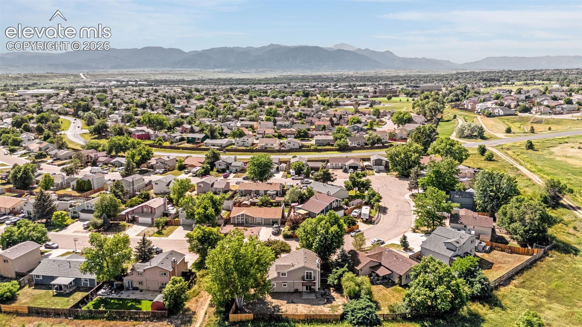 Aerial perspective featuring established residential surroundings with mature trees and a prominent mountain range backdrop