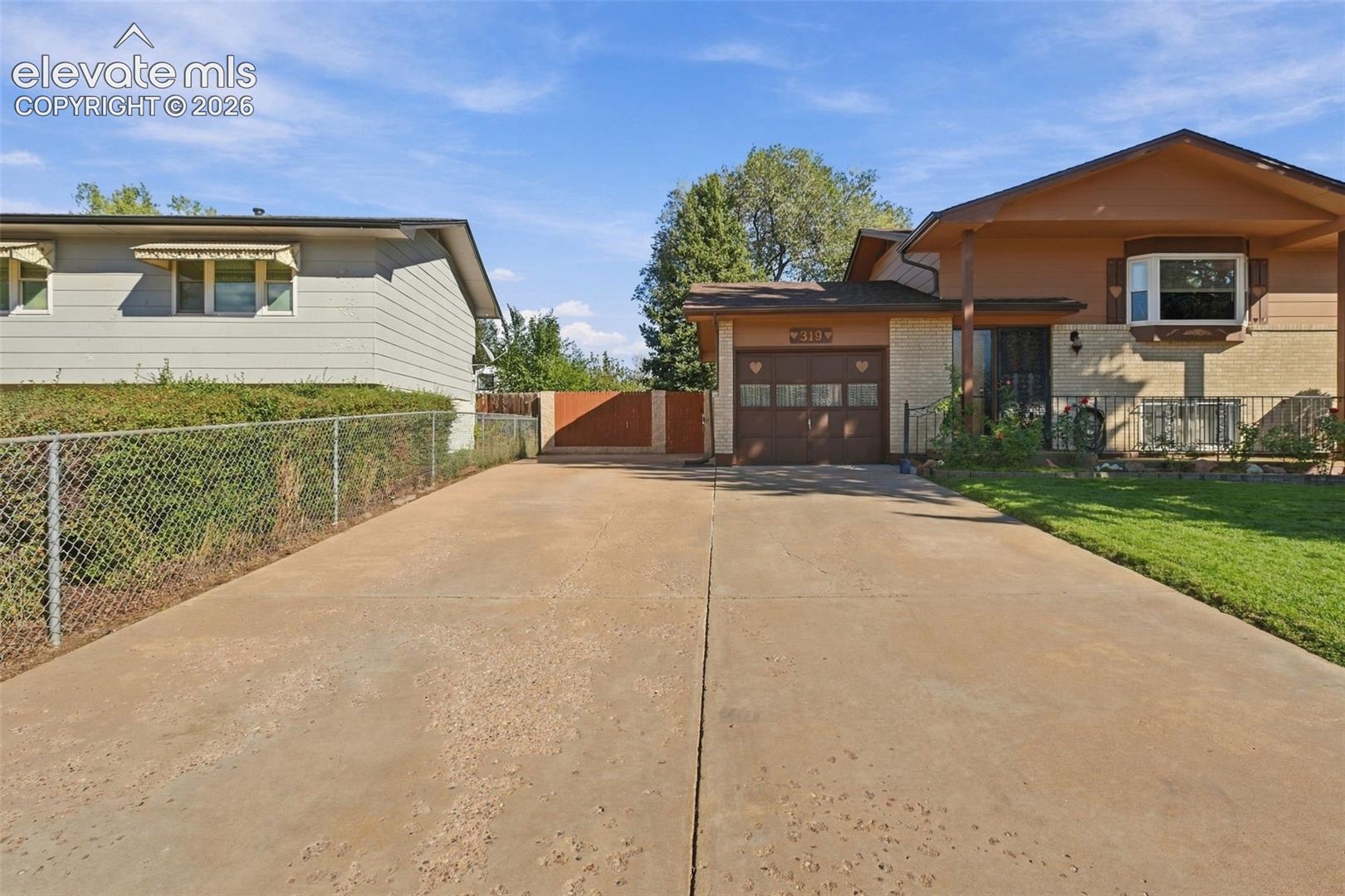 Exterior of a split-level residence featuring a multi-material facade, an attached garage with multi-pane windows, a concrete driveway, and a chain-link fence