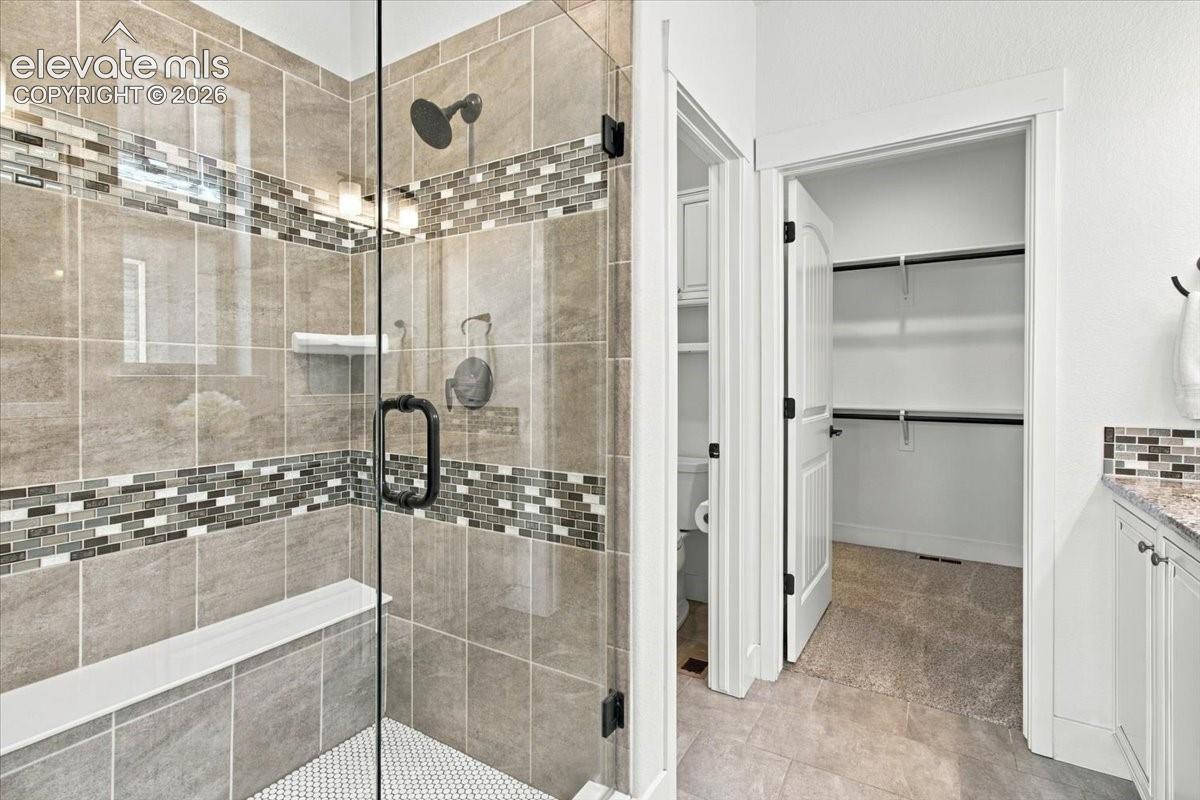 Walk-in shower featuring a frameless glass door, matte black fixtures, integrated bench, and decorative mosaic tile accents