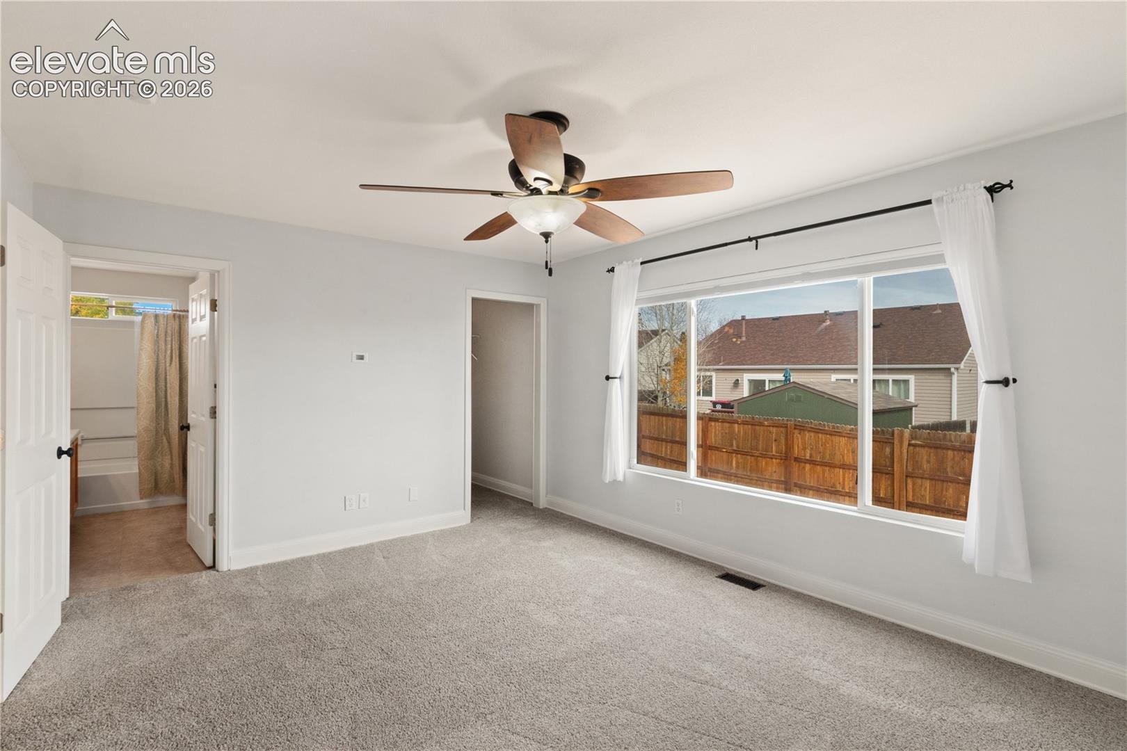 Spacious room featuring neutral carpeting, a central ceiling fan with integrated lighting, and a large picture window