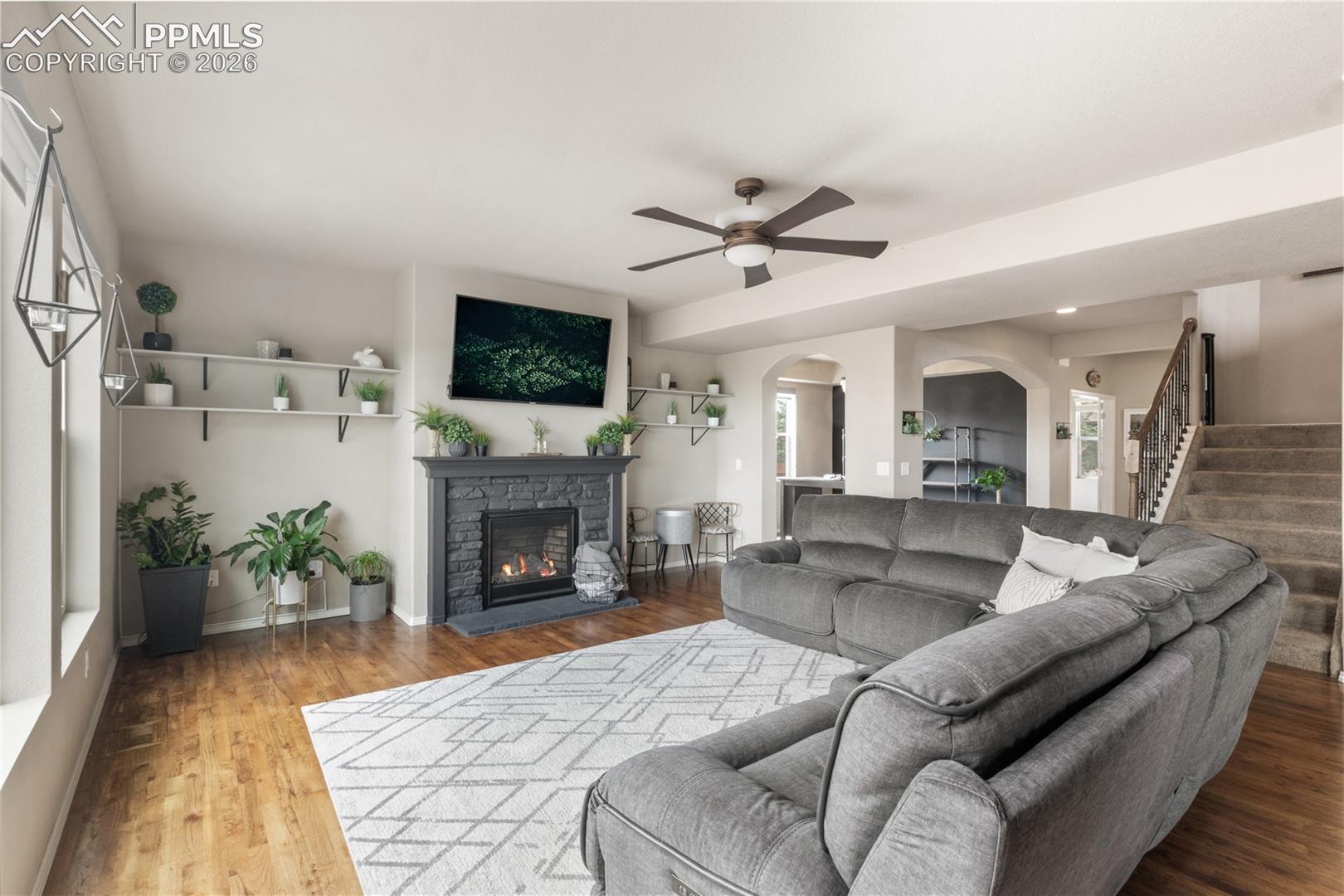 Living room featuring arched walkways, ceiling fan, light wood finished floors, and a fireplace