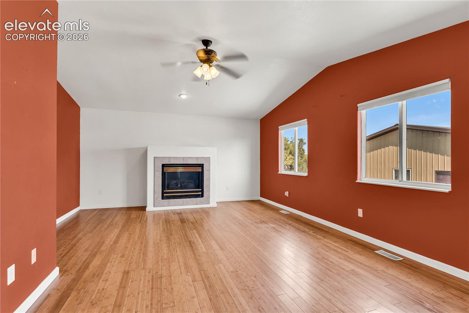 Vaulted ceiling featuring a ceiling fan, wood-finish flooring, and a fireplace with a tiled surround