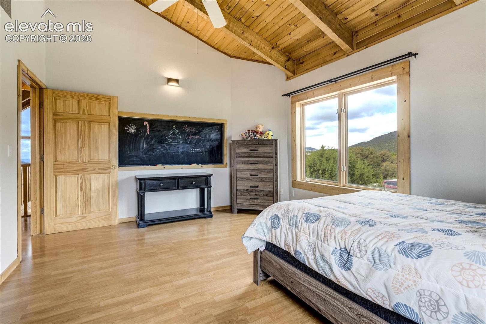Room featuring a vaulted wood-paneled ceiling, wood-finish flooring, and a large window with natural wood trim