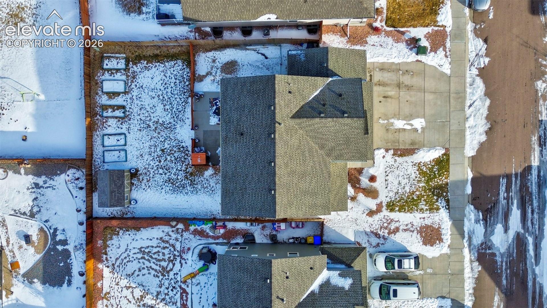 Aerial view featuring a multi-pitched shingled roof, concrete driveway, fenced yard, and detached storage structure