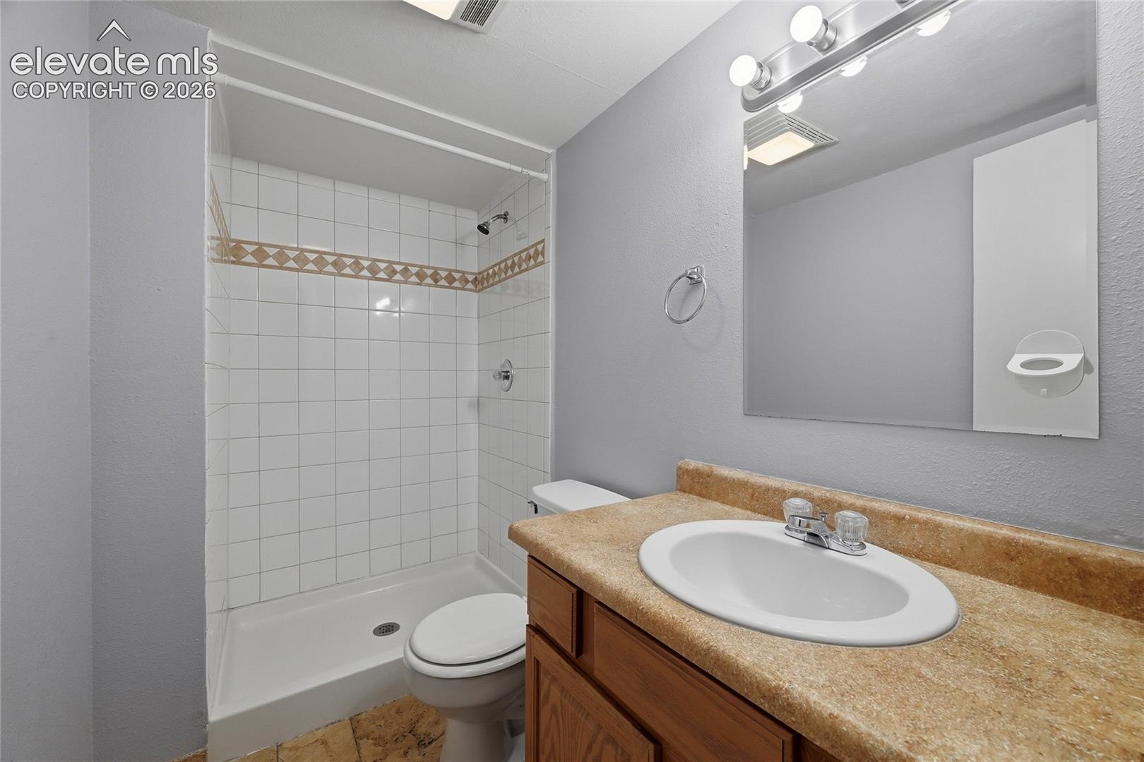 Bathroom featuring a vanity with a solid-surface countertop, an integrated oval sink, a wall-mounted mirror, and a tub-shower combination with decorative tile inlay