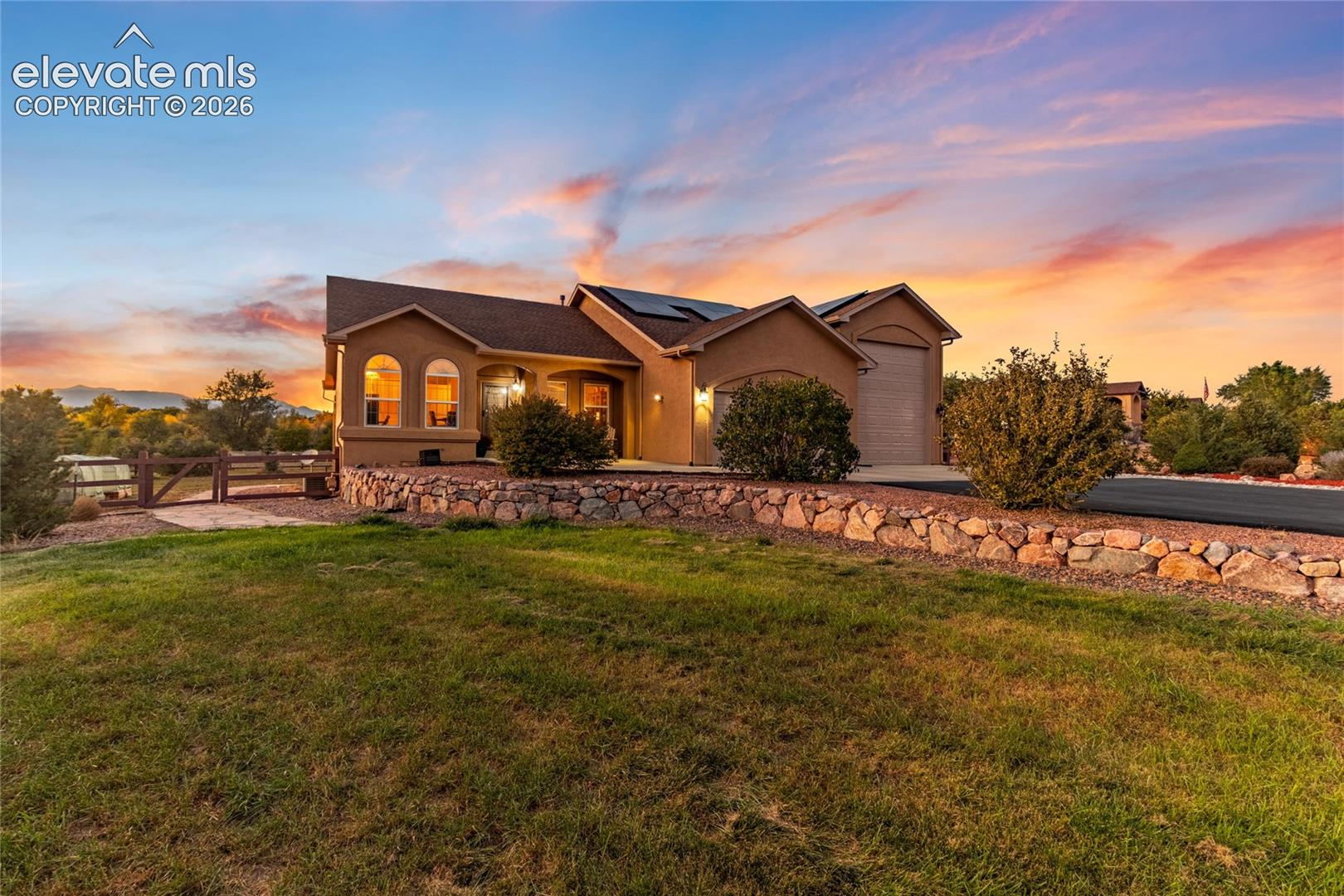 Single-story exterior featuring arched windows, stacked stone retaining wall, roof-mounted solar panels, and paved driveway