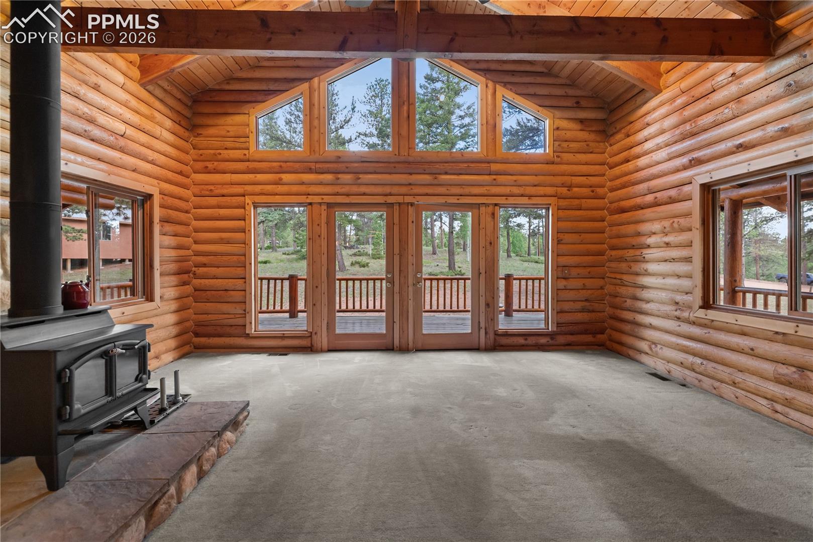 Unfurnished living room with a wood stove, a wooden ceiling with exposed beams, high vaulted ceiling, carpet floors, and log walls