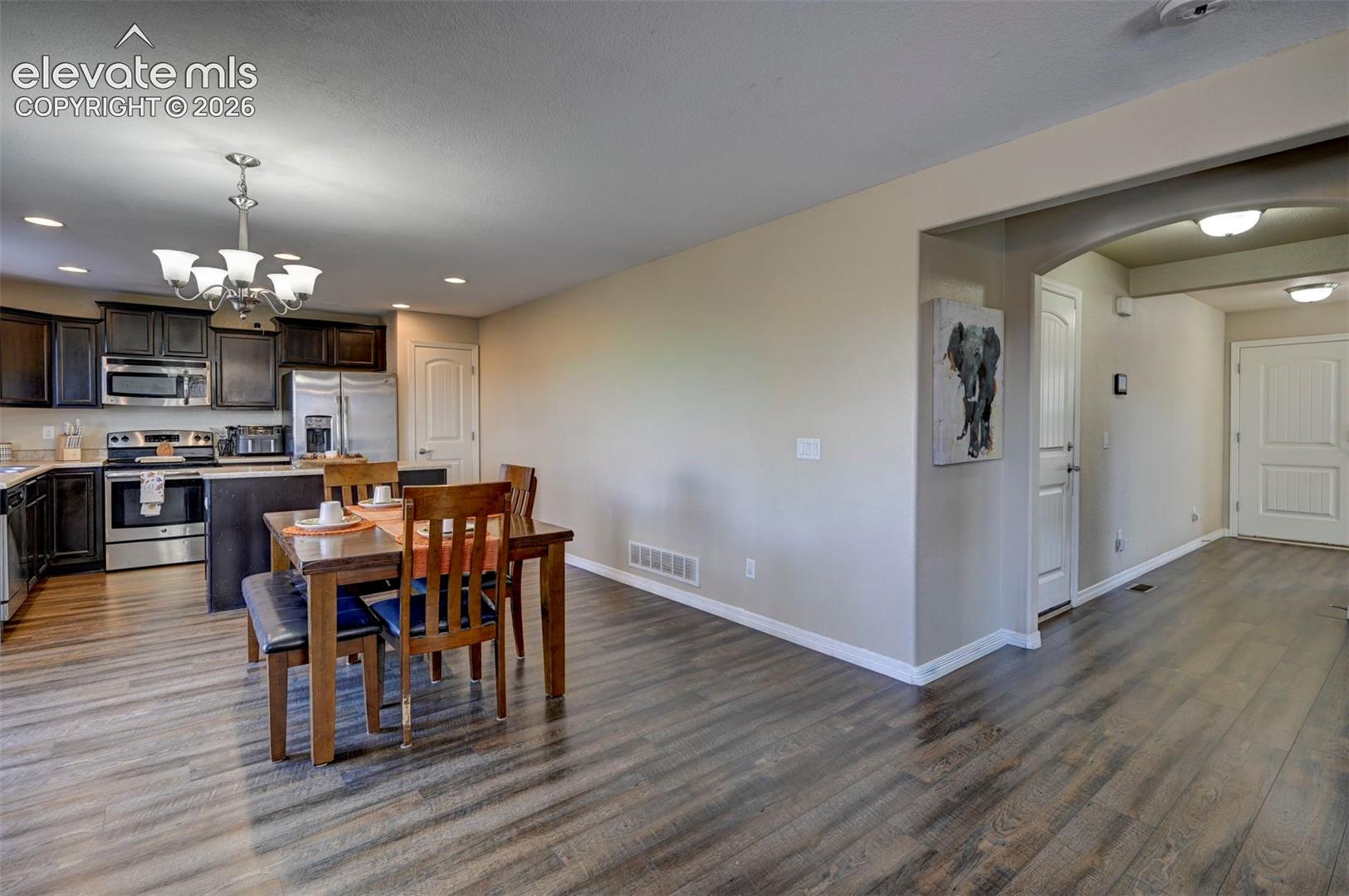Wood-finish flooring throughout, kitchen with dark wood cabinetry, stainless steel appliances, recessed lighting, and a chandelier