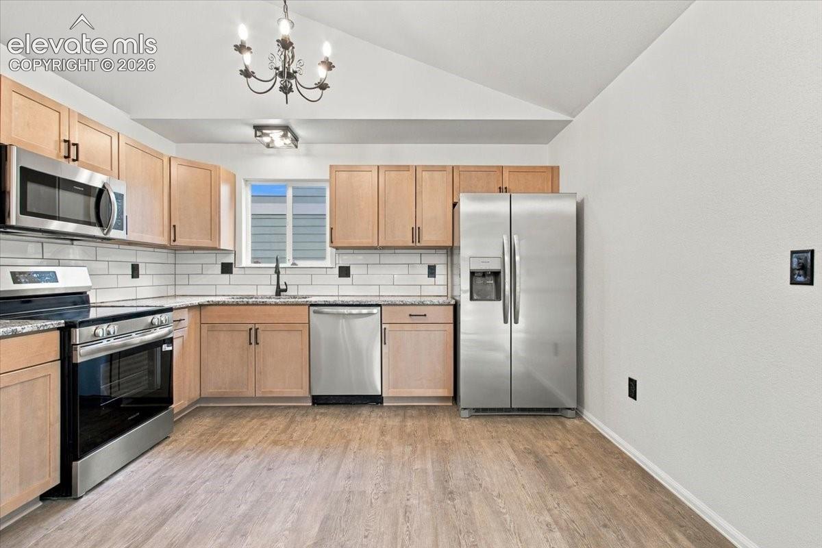 Kitchen featuring wood-finish cabinetry, stainless steel appliances, subway tile backsplash, vaulted ceiling, and wood-finish flooring