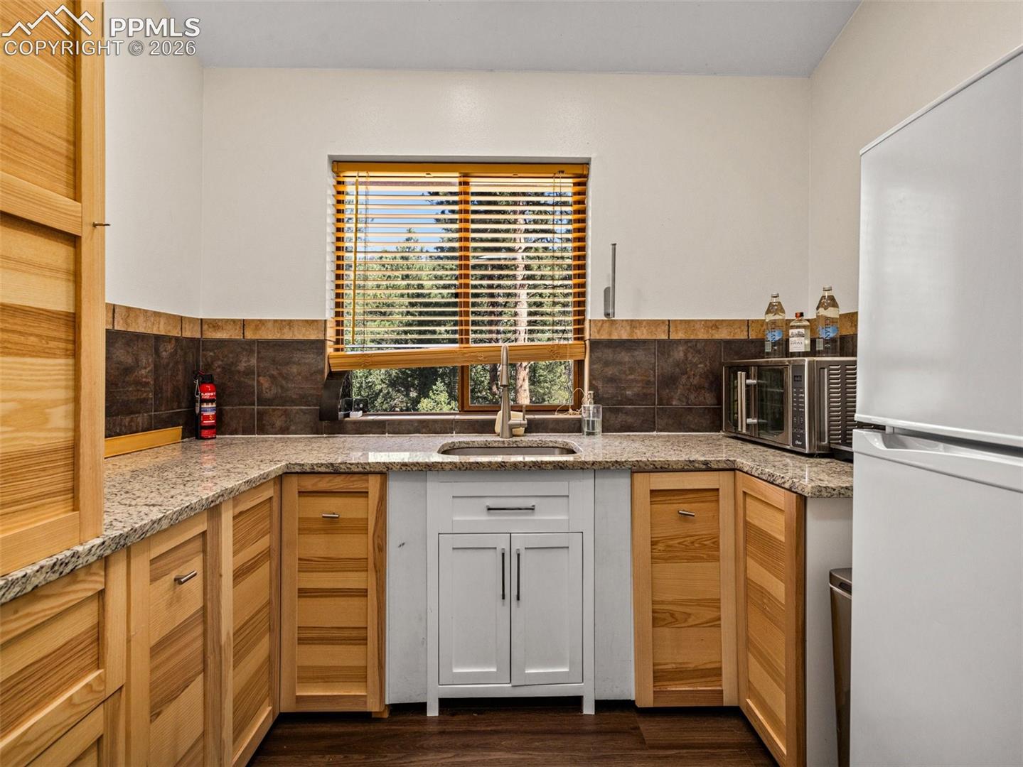 Kitchen featuring freestanding refrigerator, light stone countertops, dark wood finished floors, and stainless steel microwave