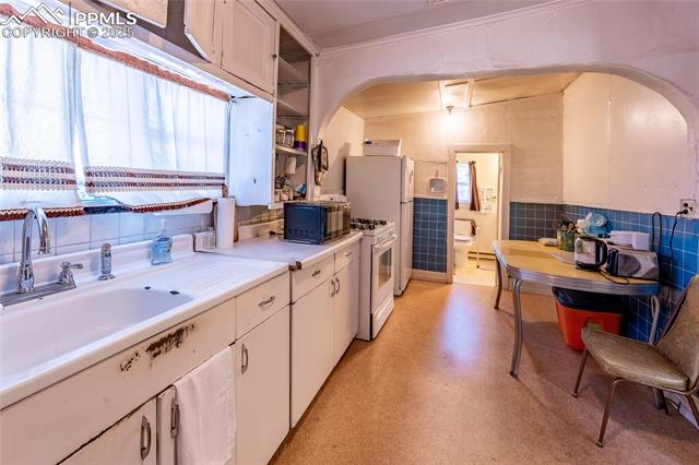 Kitchen featuring light countertops, white gas stove, open shelves, tile walls, and plenty of natural light