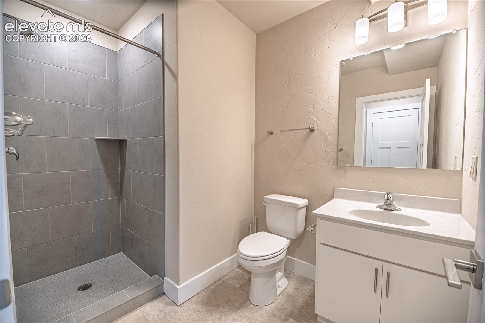 Bathroom featuring a tiled shower with a built-in niche, white vanity with an integrated sink, rectangular mirror, and three-light fixture