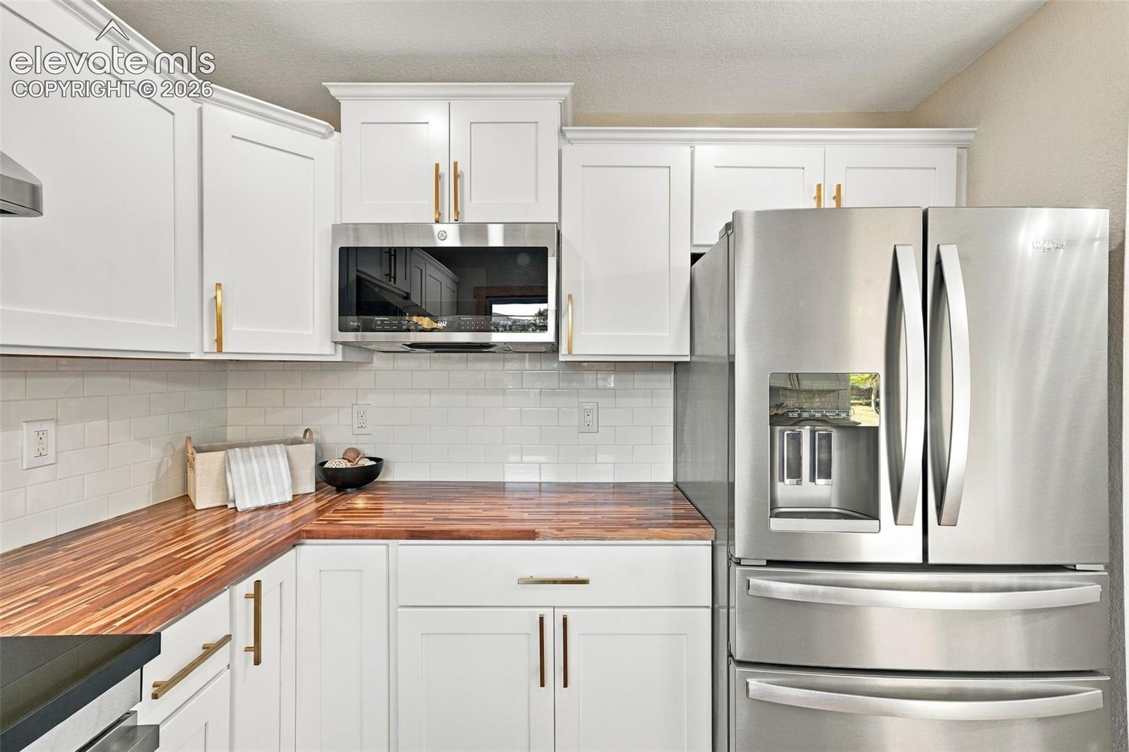 White Shaker-style cabinetry featuring gold-tone hardware, wood-finish countertops, subway tile backsplash, and stainless steel appliances