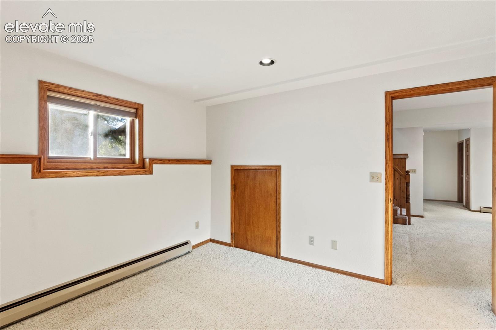 Room featuring neutral wall-to-wall carpeting, wood trim casing around the window and doorways, recessed lighting, and a built-in access panel
