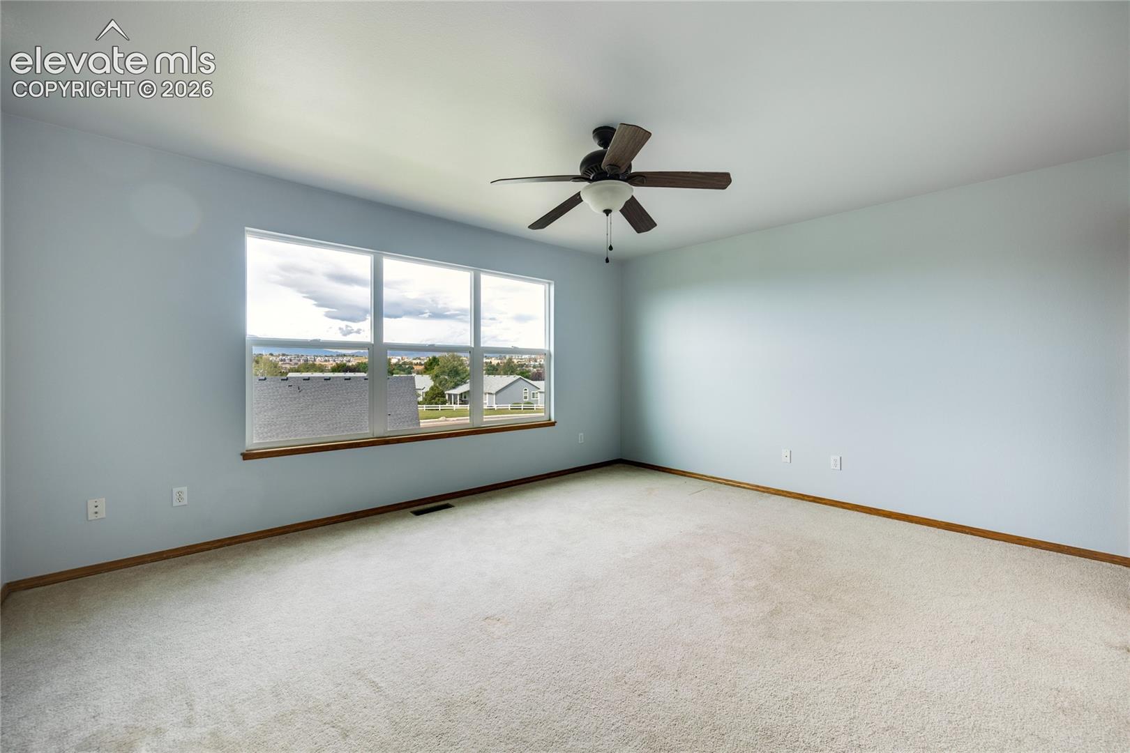 Expansive room featuring light-colored carpeting, a multi-pane window with a wood-finish sill, and a ceiling fan with integrated lighting
