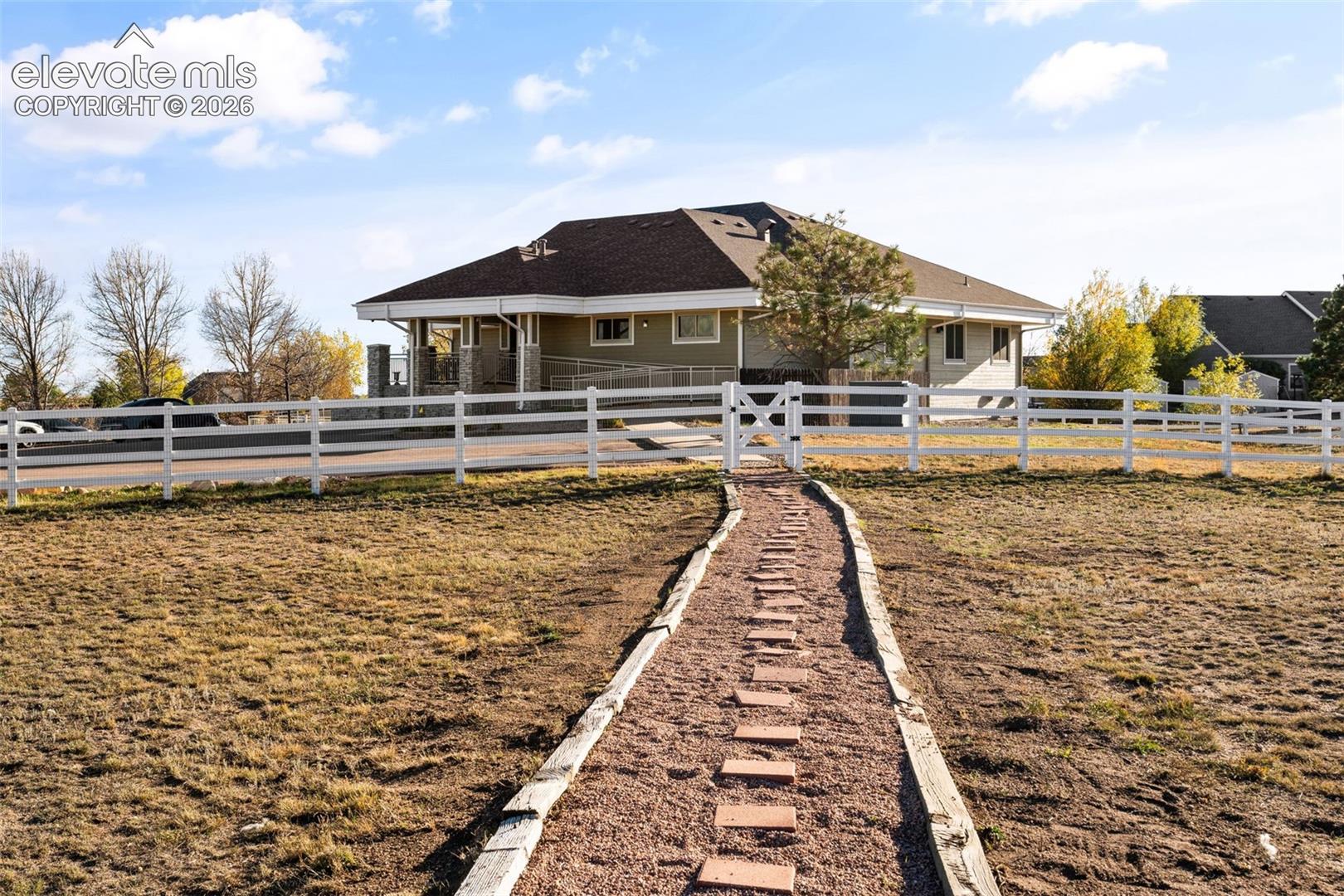 Single-story home featuring a low-slope roof, white three-rail fencing, a stone-lined gravel walkway, and stone exterior pillar detailing