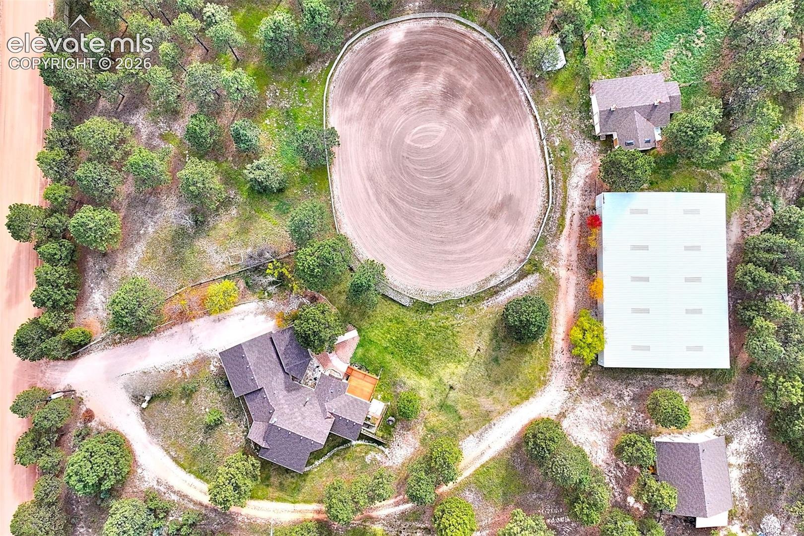 Aerial property featuring a riding arena, a large detached outbuilding, multiple structures, and expansive acreage forested with mature trees