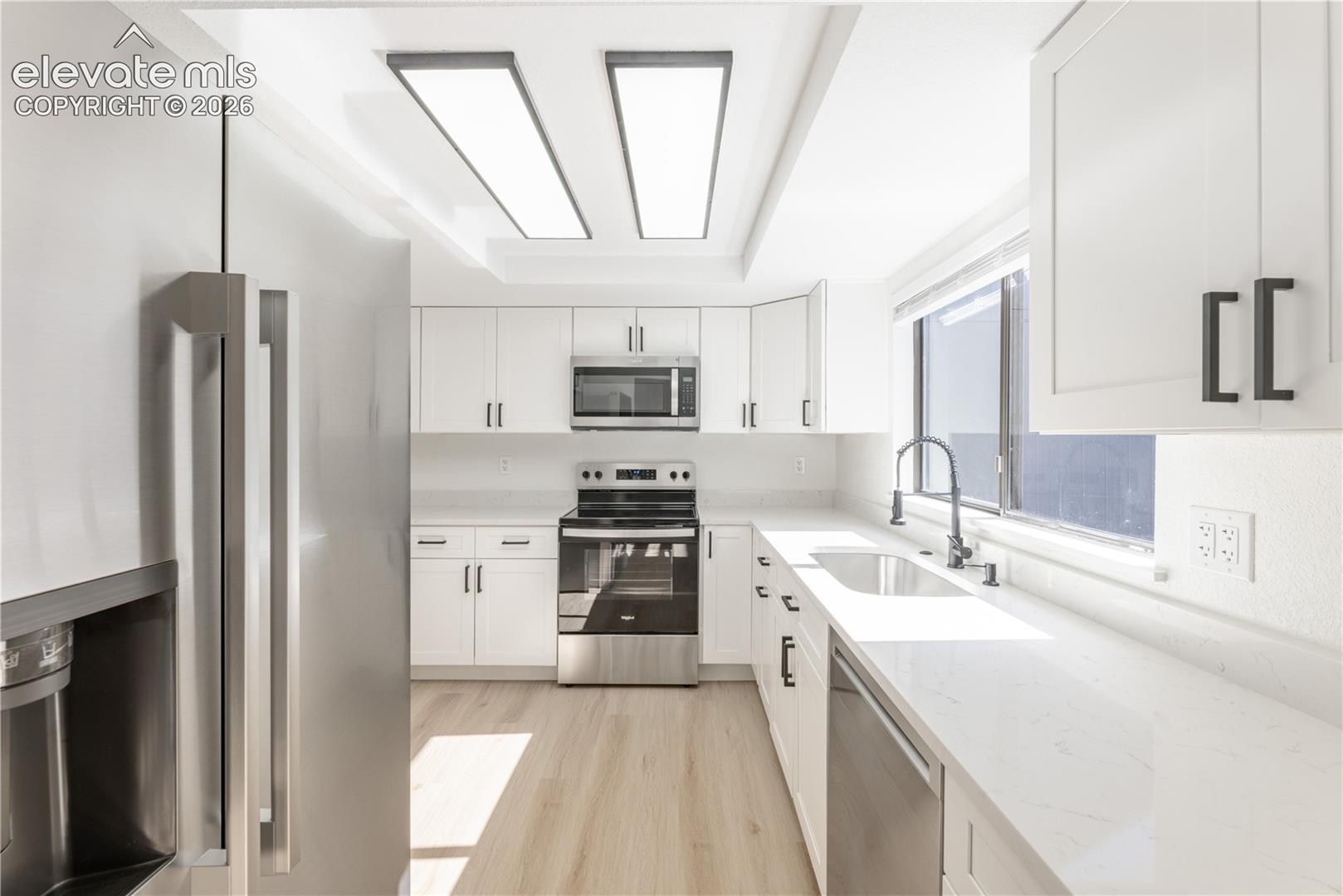 Kitchen featuring shaker-style white cabinetry, quartz countertops, stainless steel appliances, wood-finish flooring, and dual rectangular flush-mount ceiling light fixtures