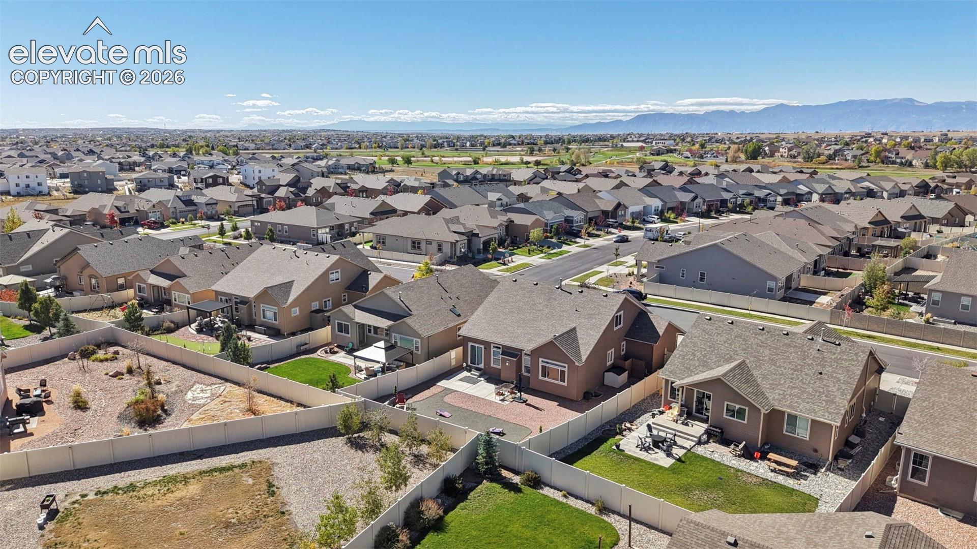 Aerial perspective of the residential property featuring a paver patio, fenced rear yard, and mountain backdrop