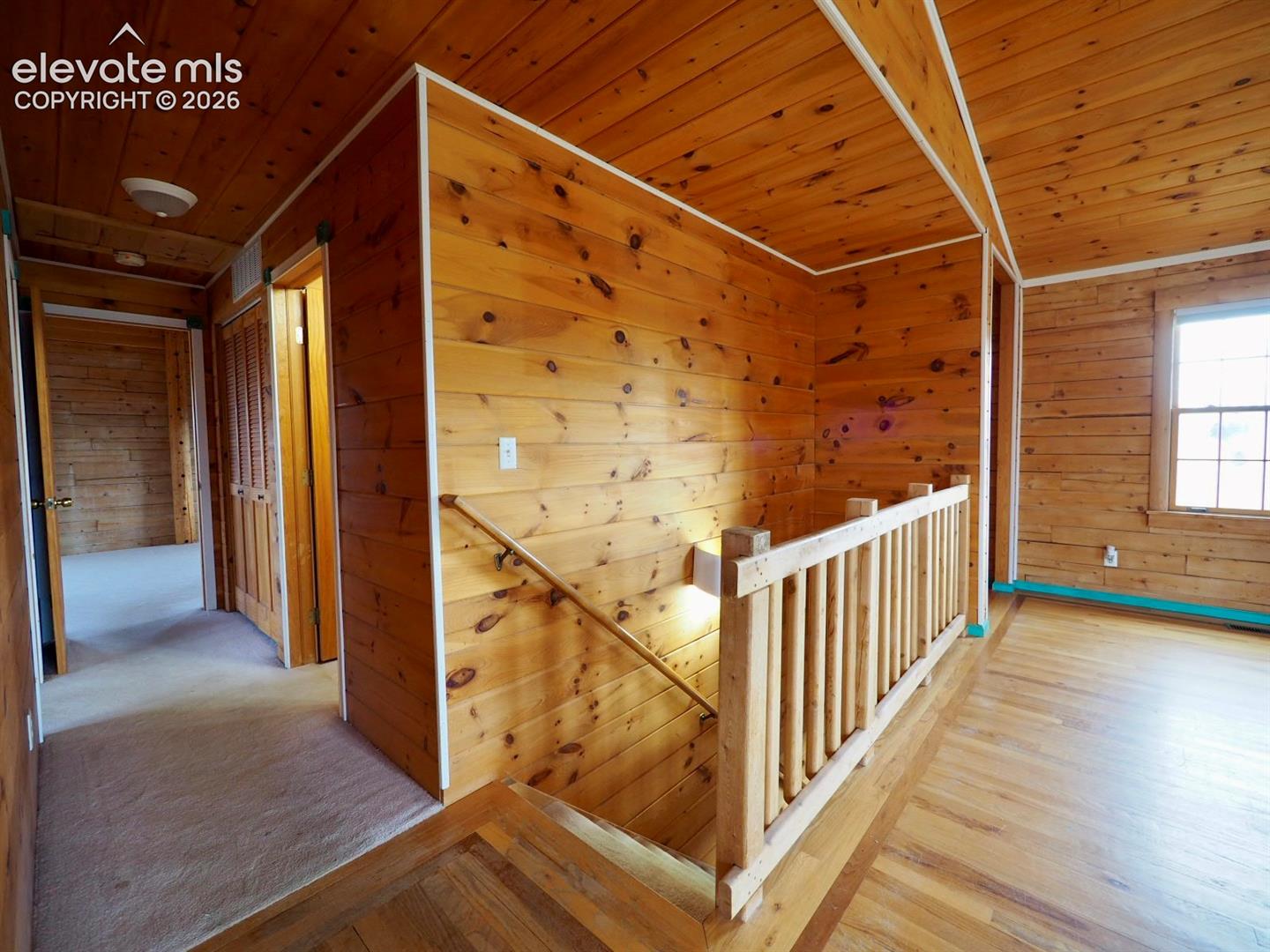 Wood-paneled interior walls and ceiling, solid wood-finish flooring, and natural wood balustrade featuring a vertical post railing