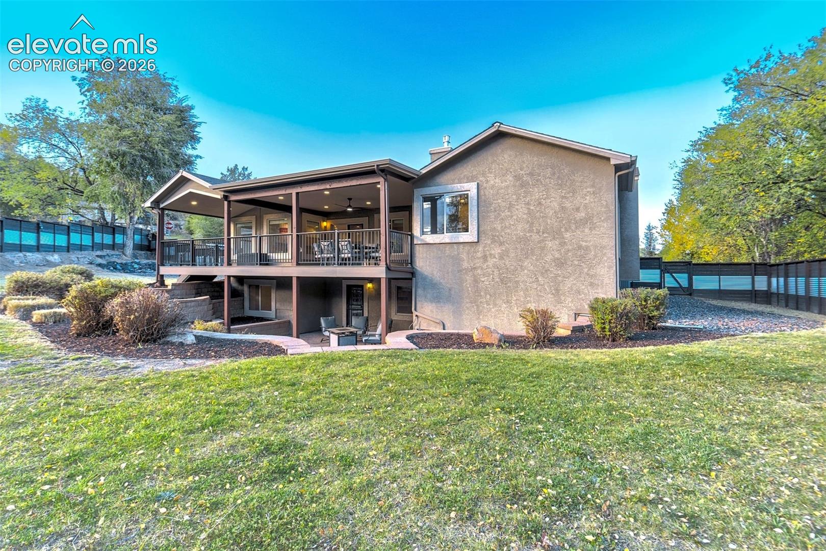 Stucco exterior residence featuring an elevated covered deck with metal railing, a lower-level concrete patio, and fenced perimeter