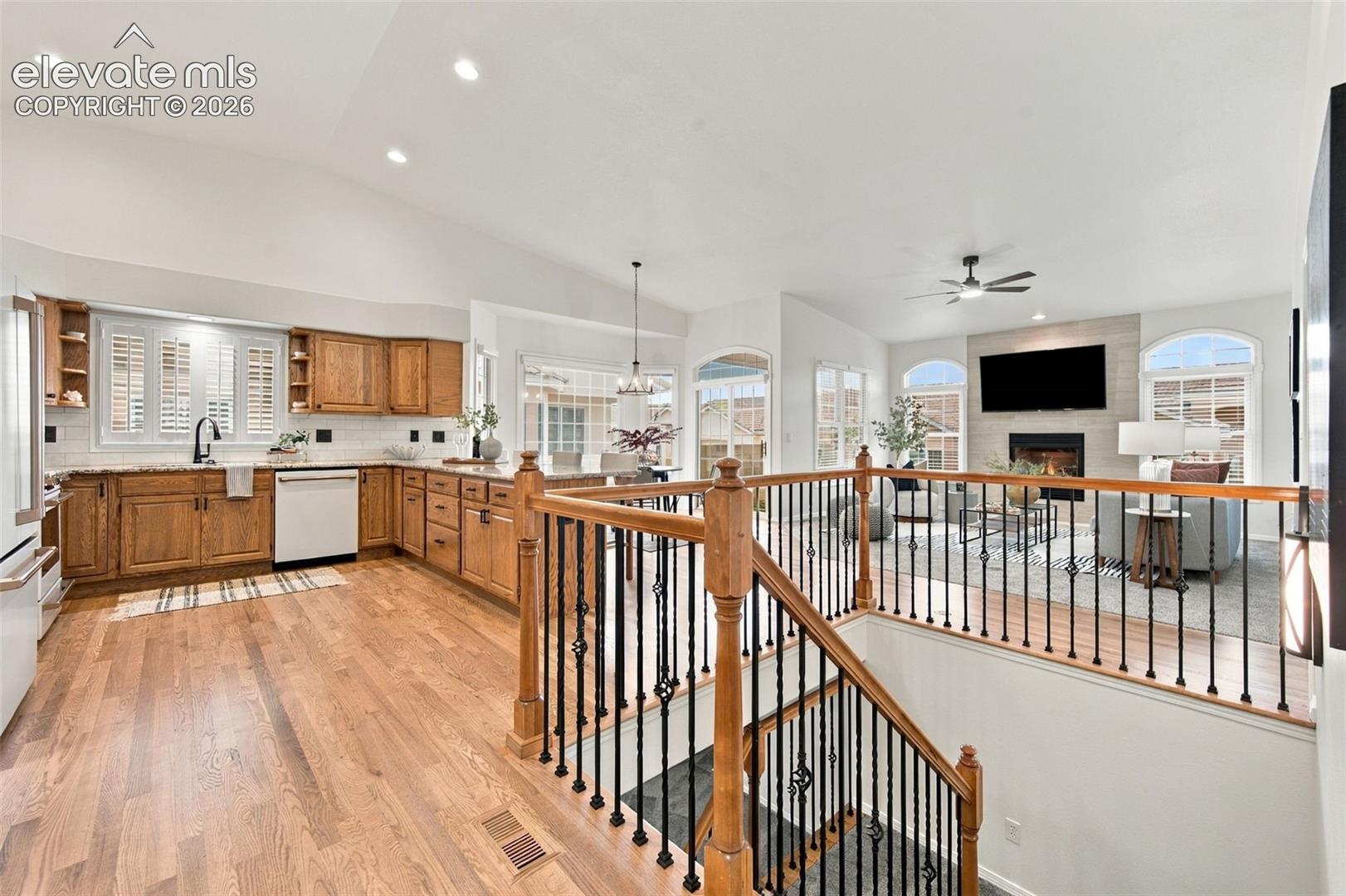 Open-concept floor plan featuring vaulted ceilings, wood-finish flooring, custom wood cabinetry, and a fireplace with decorative tile surround