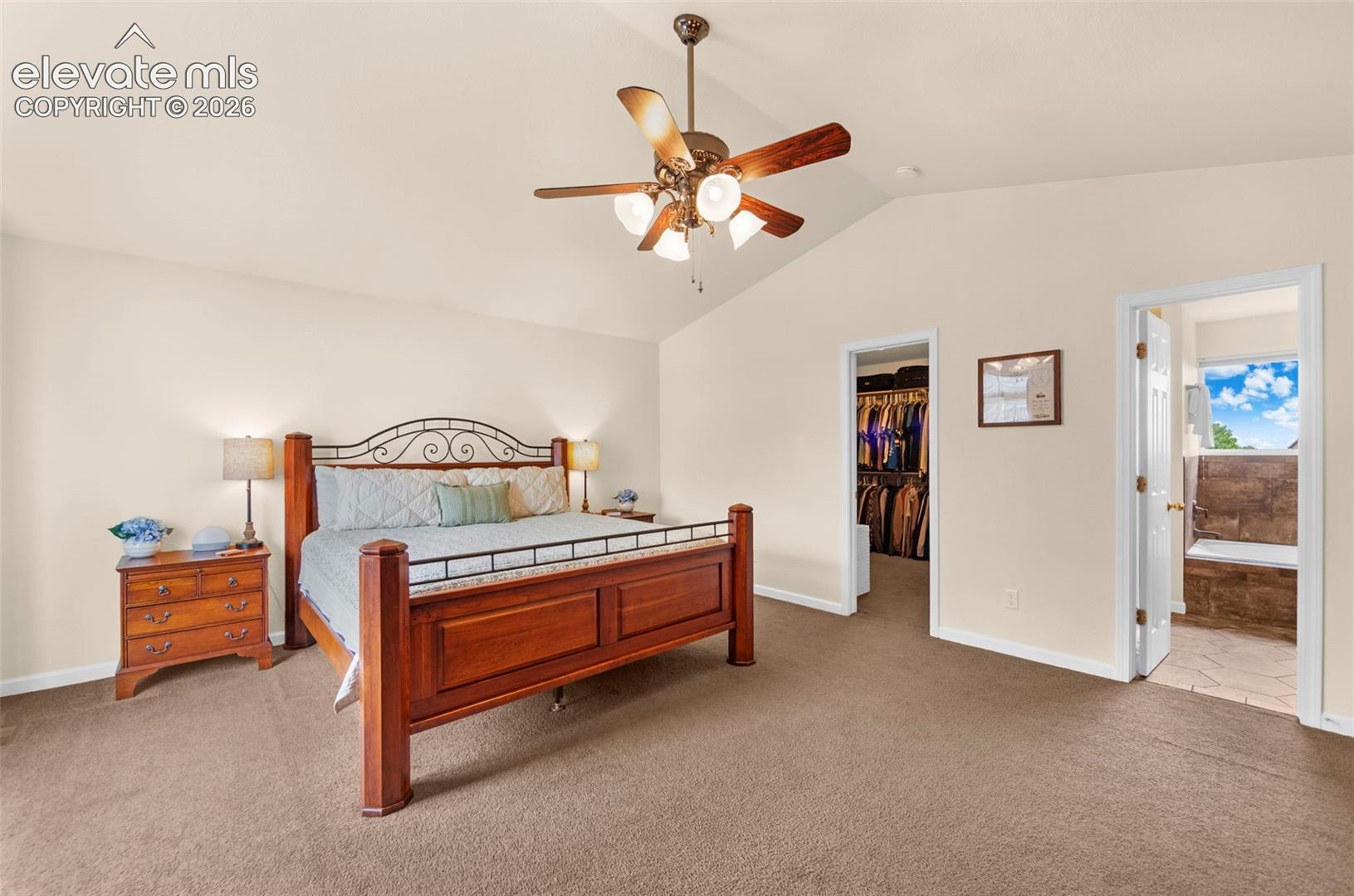 Spacious room featuring vaulted ceilings, a ceiling fan, plush carpet flooring, a walk-in closet, and an attached bath with a built-in tub