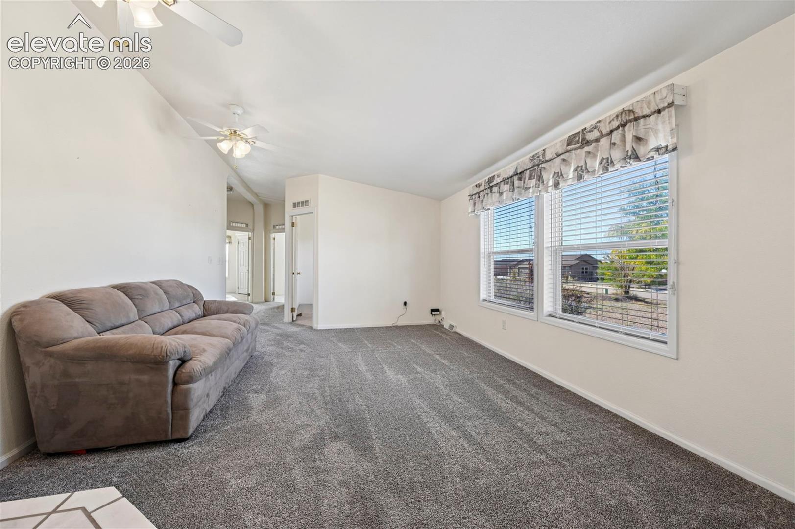 Vaulted ceilings, dual ceiling fans, wall-to-wall carpeting, and expansive windows with blinds