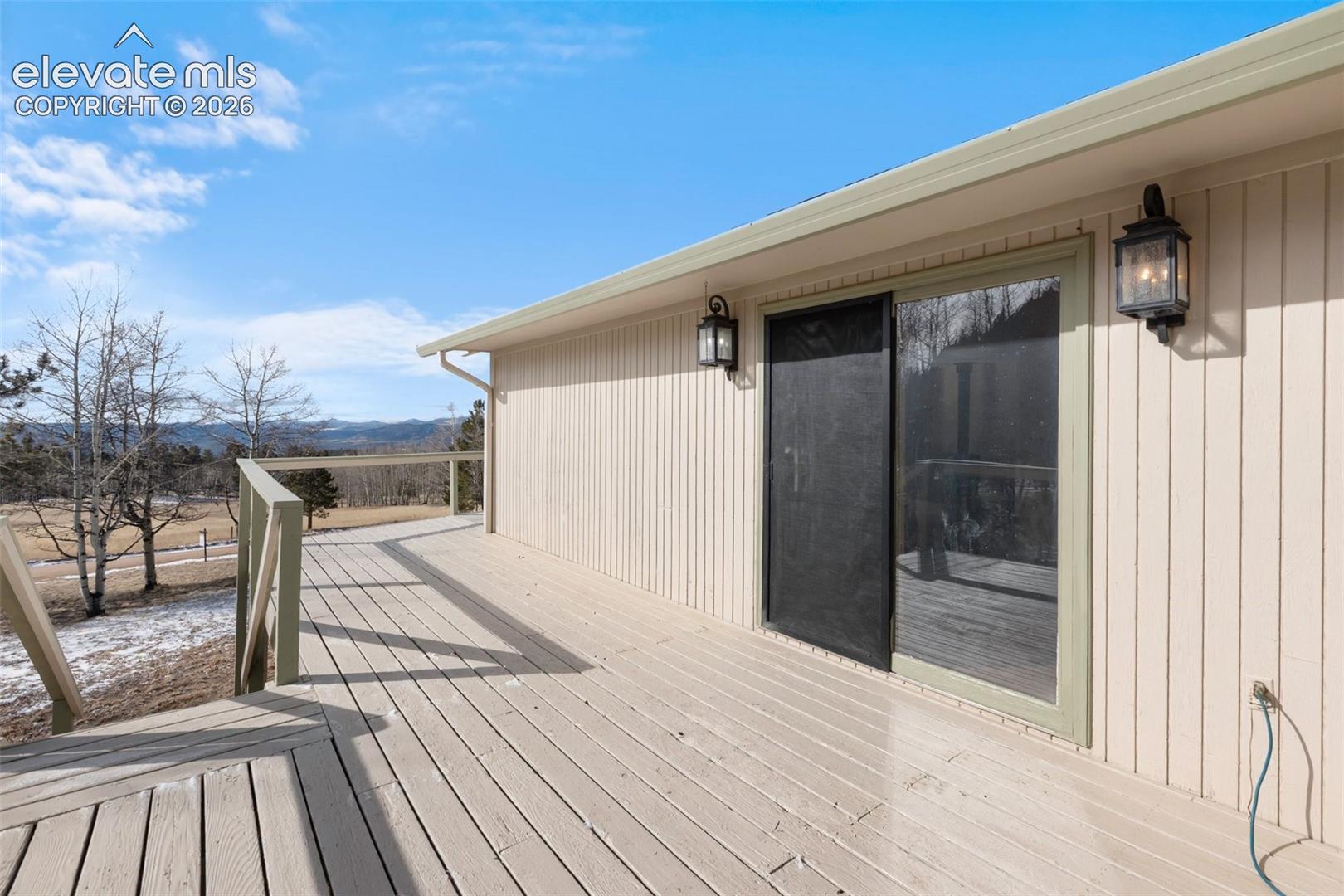 Expansive wood-finish deck with railing, exterior wall lanterns, and sliding glass door with screen