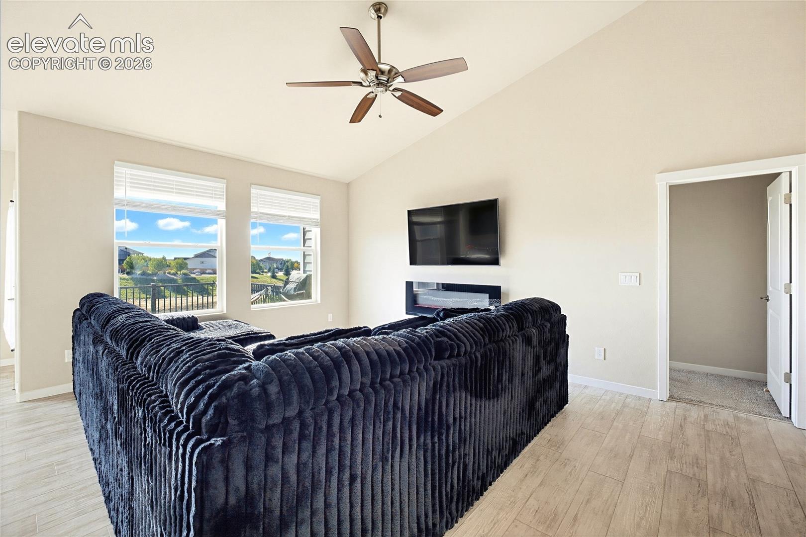 Vaulted ceilings, wood-finish flooring, wall-mounted electric fireplace, and a ceiling fan