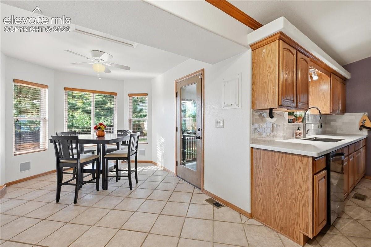 Kitchen featuring wood-finish cabinetry, light-toned countertop, stainless steel sink with gooseneck faucet, and tile flooring