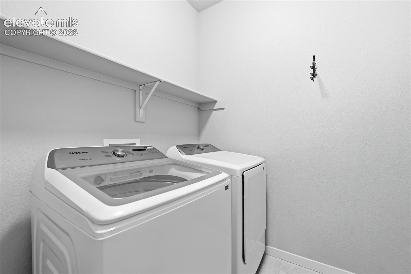 Laundry area featuring a wall-mounted shelf, light-toned walls, and a multi-prong hook fixture.