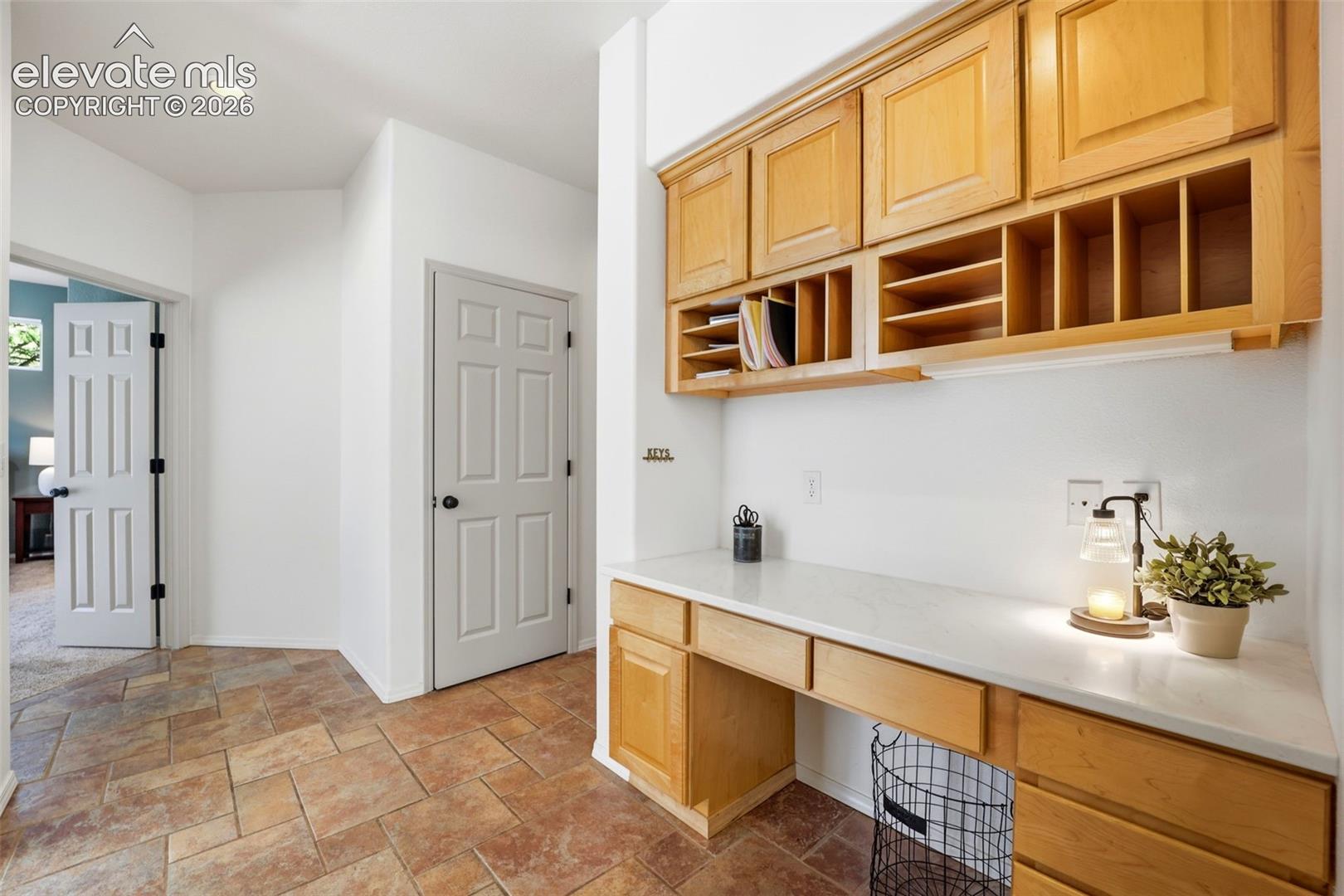 Built-in desk area with light wood-finish cabinetry, integrated shelving, white countertop, and tiled flooring