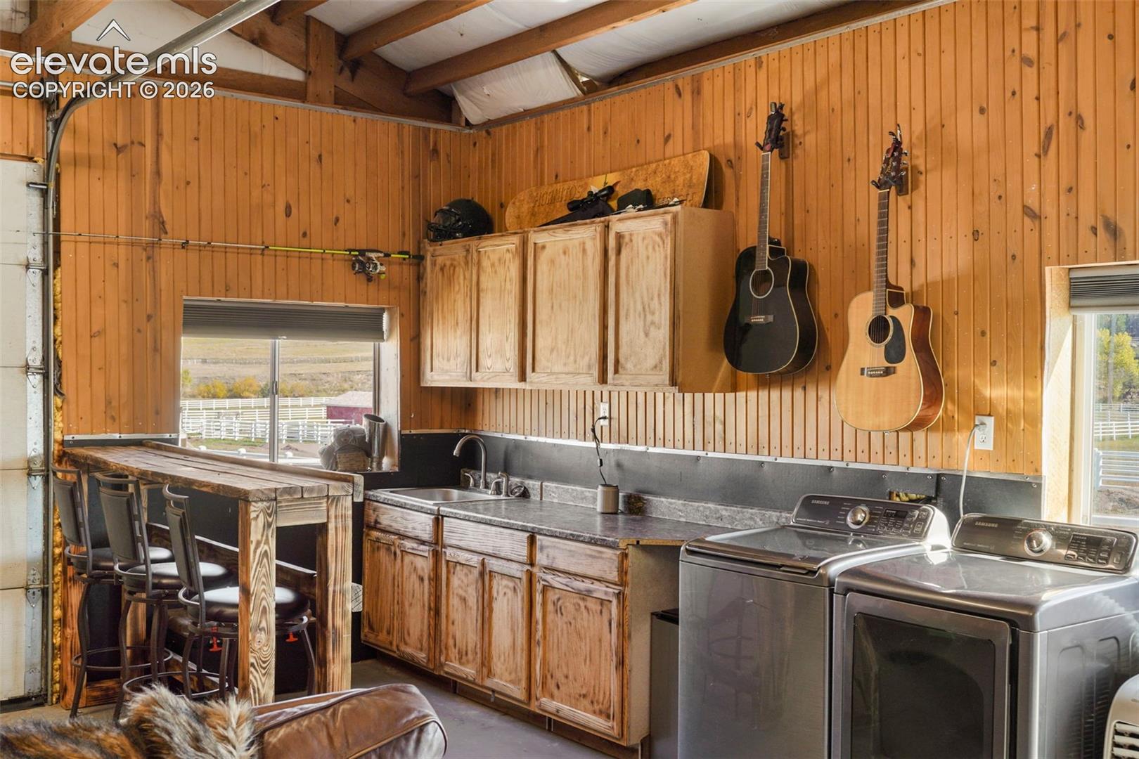 Wood-paneled interior featuring a built-in bar, stainless steel washer and dryer, and upper and lower cabinetry with a sink