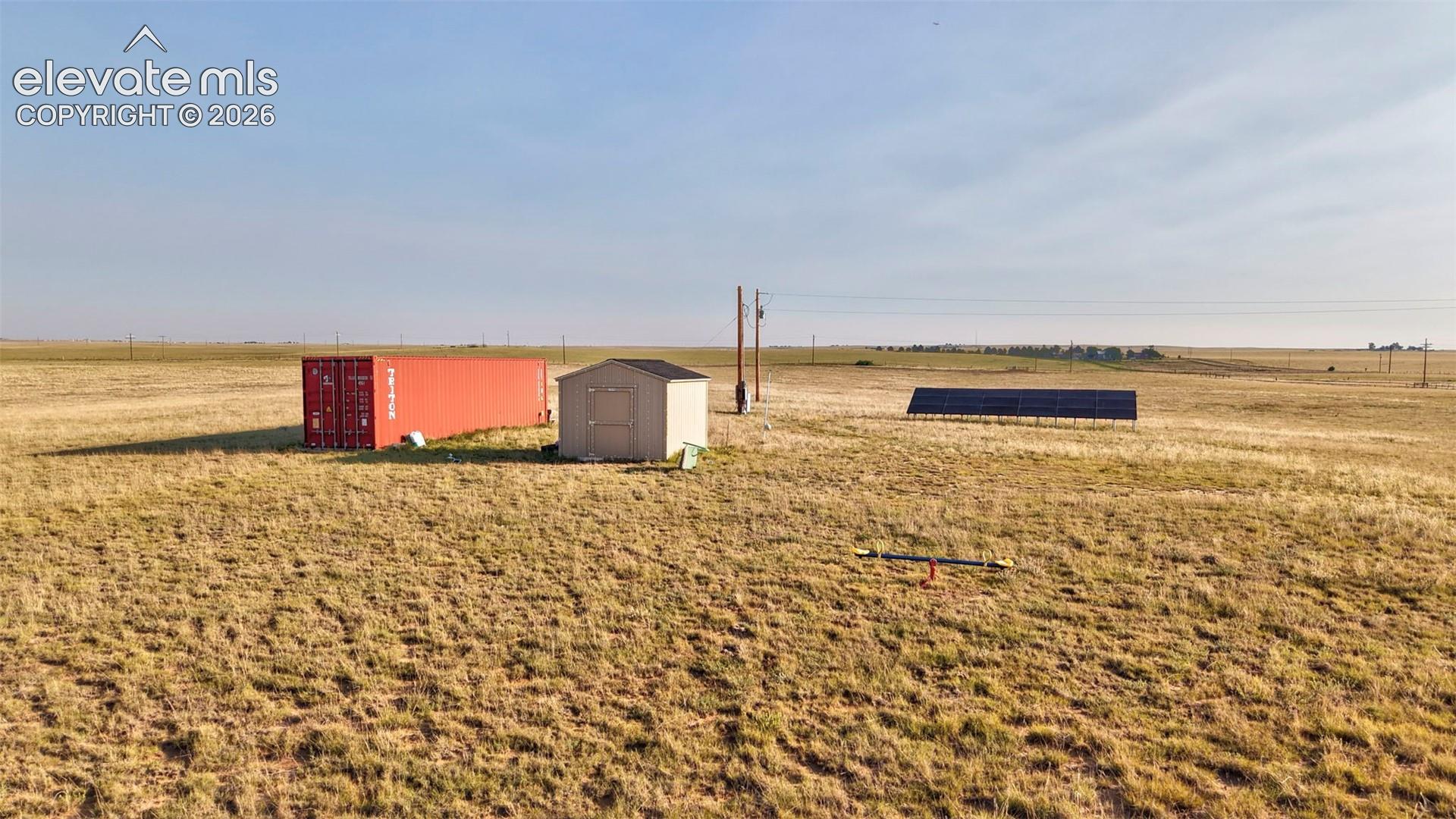 Expansive open land featuring a red storage container, a utility shed, and ground-mounted solar panels