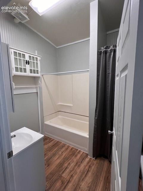 Bathroom featuring wood-finish flooring, a white vanity cabinet with an integrated sink, and an elevated wall-mounted cabinet with glass-panel doors