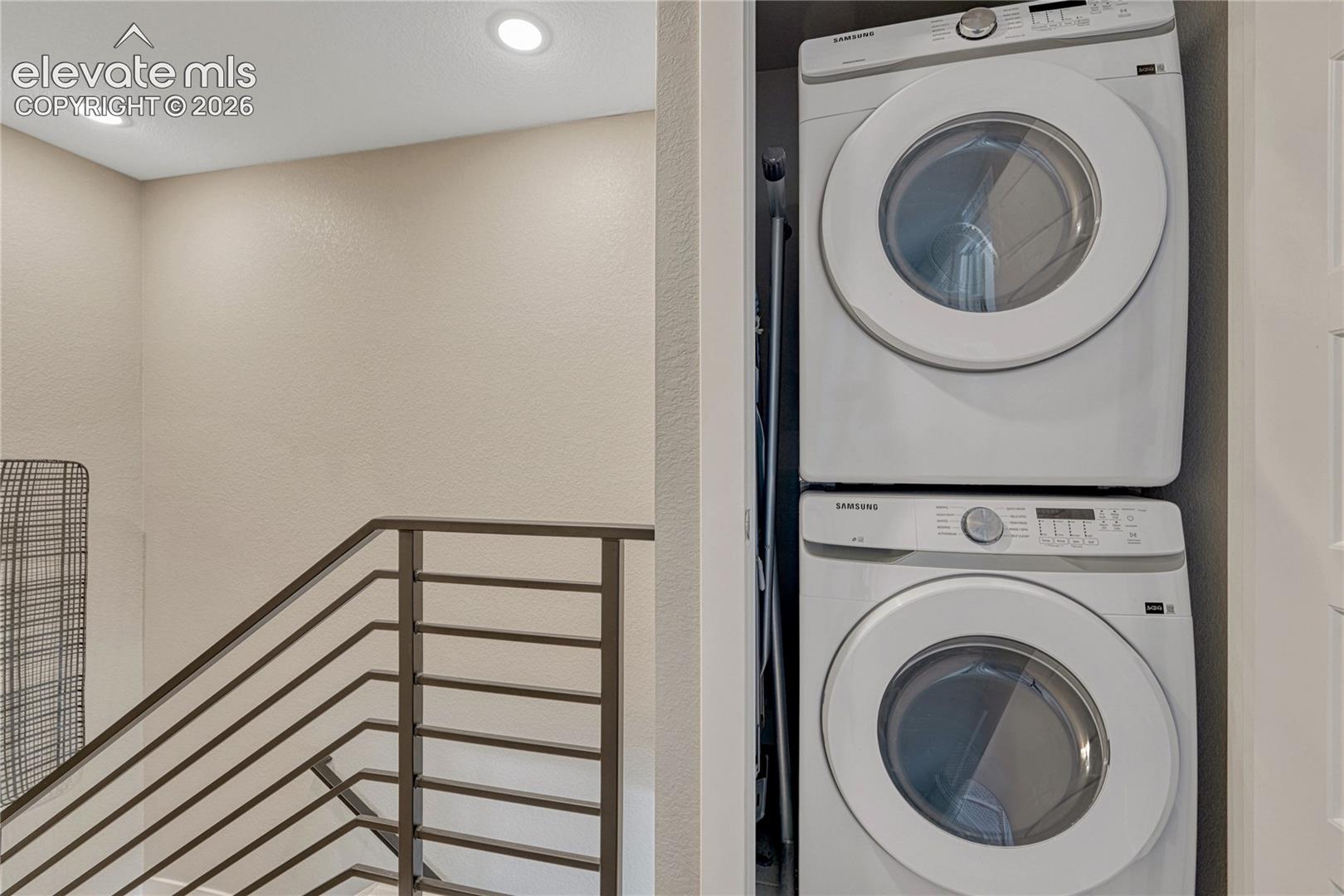 Stacked laundry appliance set housed within a built-in closet, complemented by recessed ceiling lighting and a metal railing system
