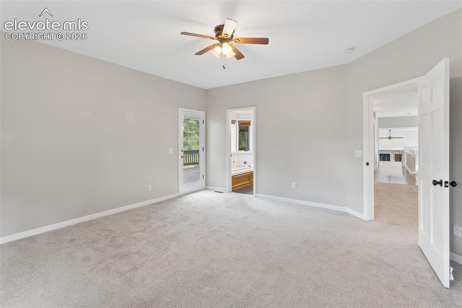 Ceiling fan with integrated lighting, light gray carpet flooring, white paneled interior doors, and a glass-paneled exterior door leading to a wooden deck