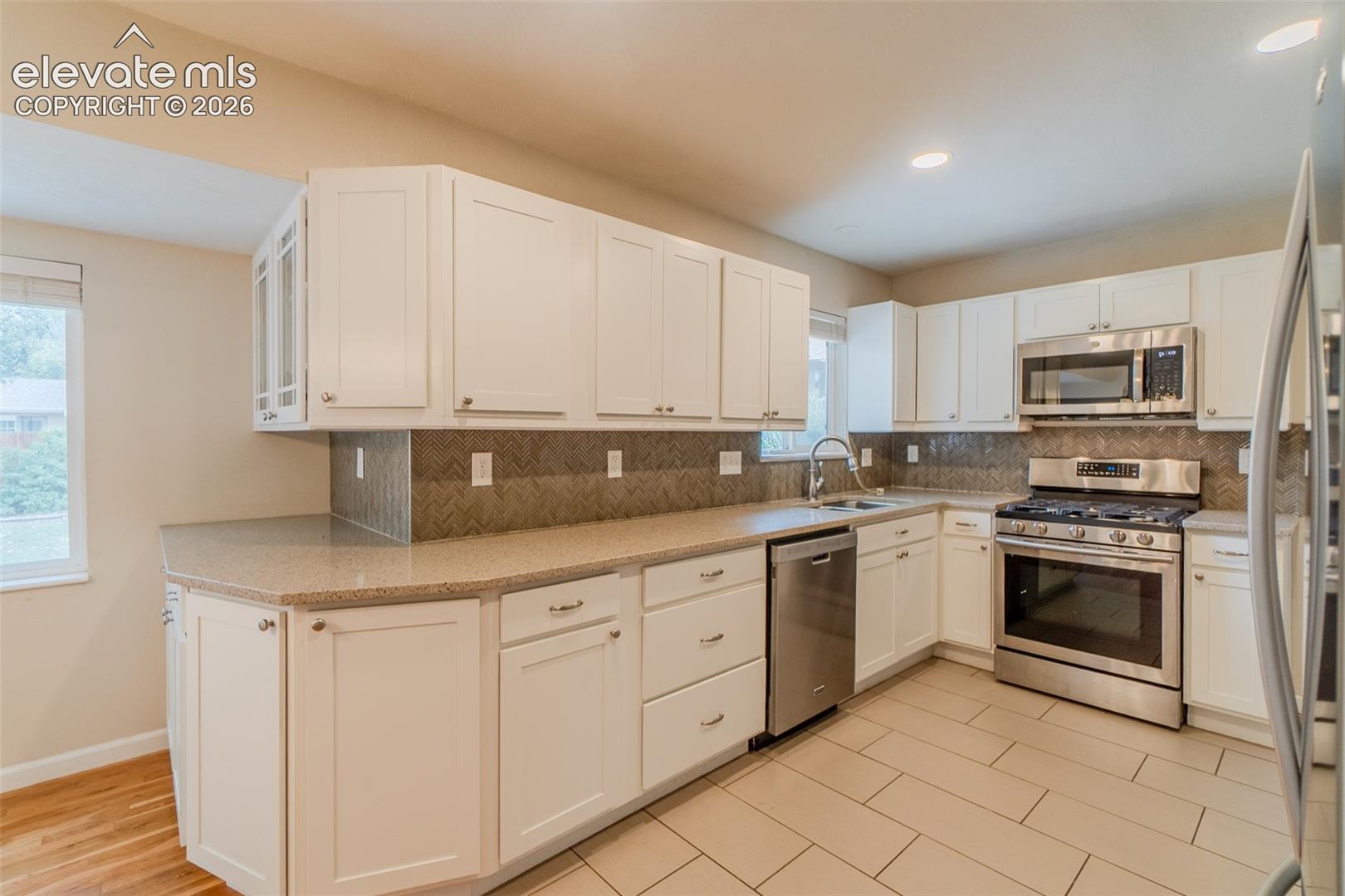 White cabinetry, stainless steel appliances, tiled backsplash, light-toned countertops, and light-toned floor tiles