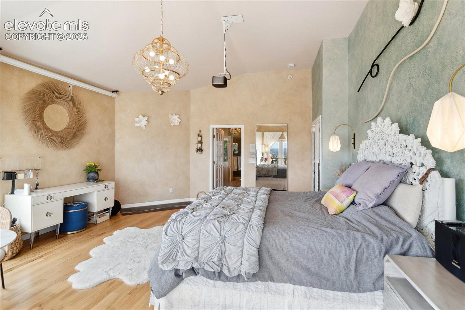 Spacious room featuring vaulted ceilings, light wood-finish flooring, two distinct accent walls, and an ornate gold-finish chandelier