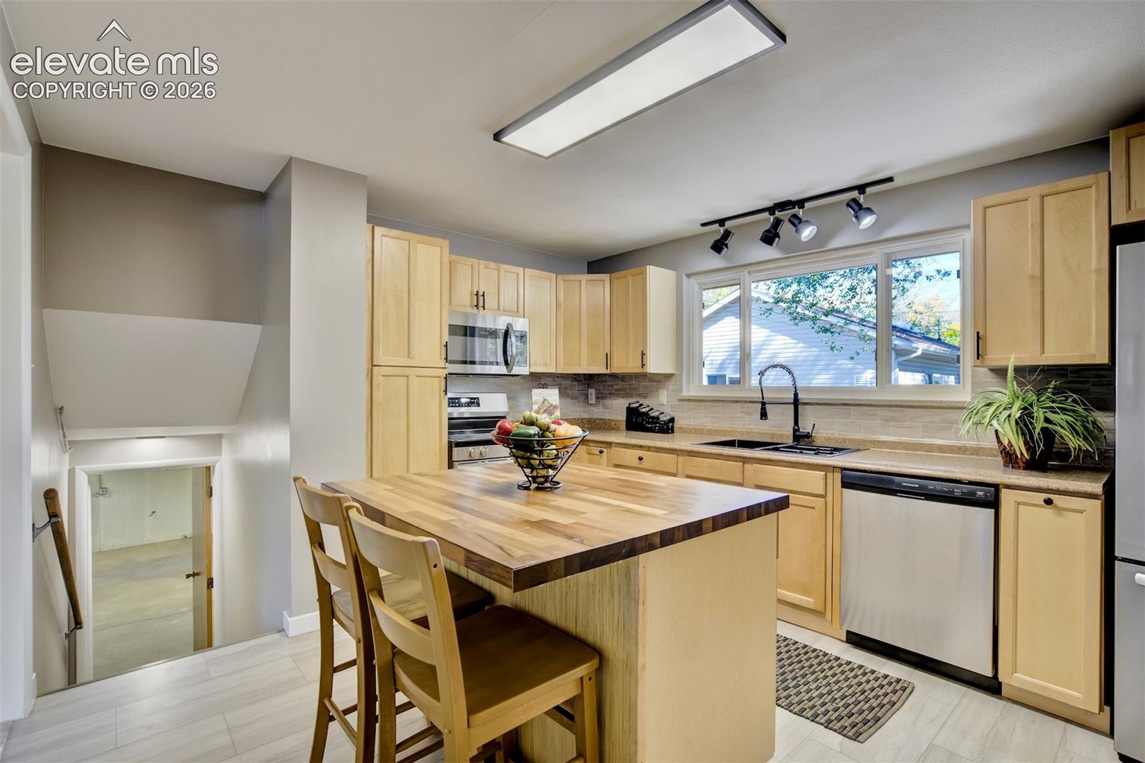 Kitchen featuring light wood cabinetry, butcher-block island countertop, stainless steel appliances, matte black faucet, and recessed and track lighting