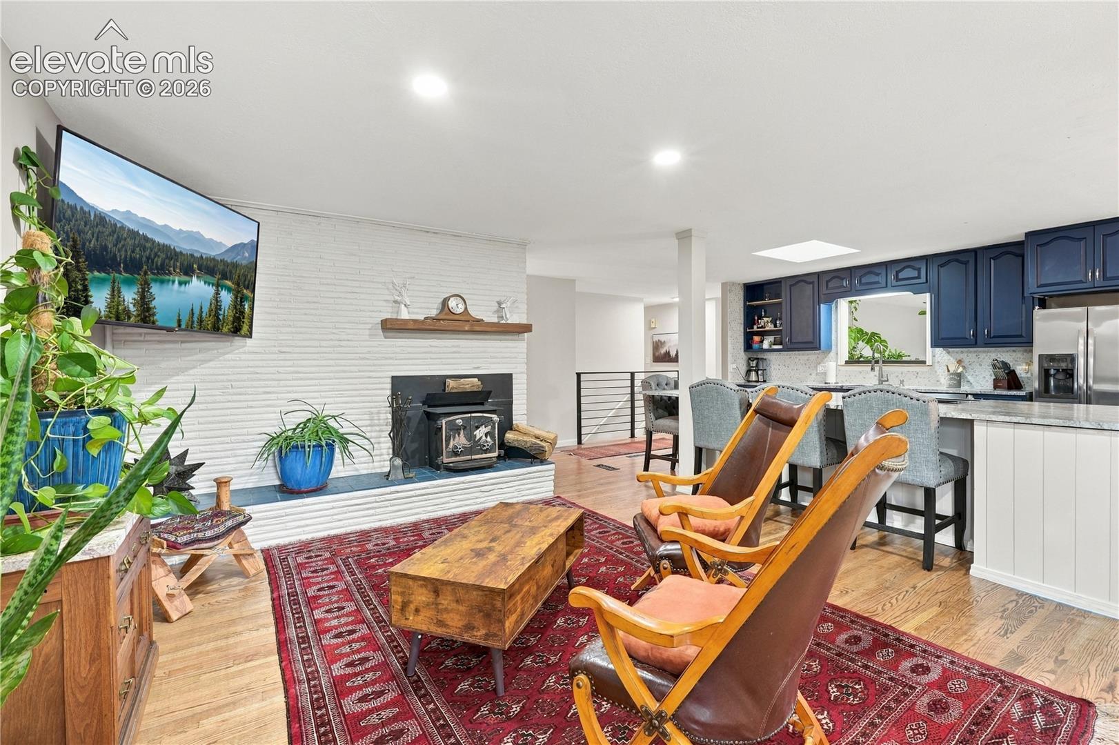 Open-concept living space featuring a white-painted brick fireplace with a wood-finish mantel and a cast-iron stove insert